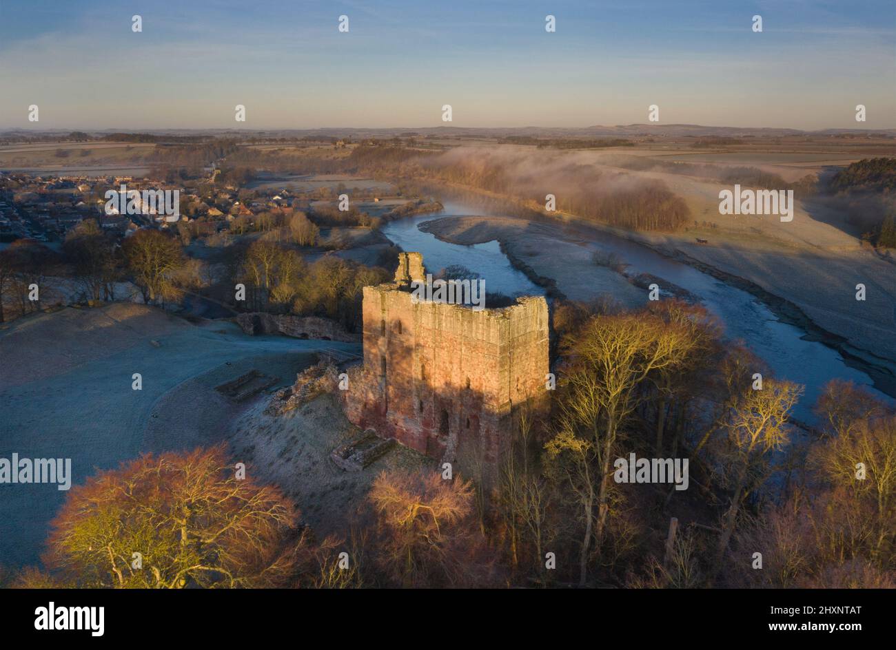 Temprano por la mañana, amanecer helado, vistas de los aviones no tripulados sobre el castillo de Norham, el pueblo de Norham y el río Tweed, Berwick, Northumberland, Inglaterra Foto de stock