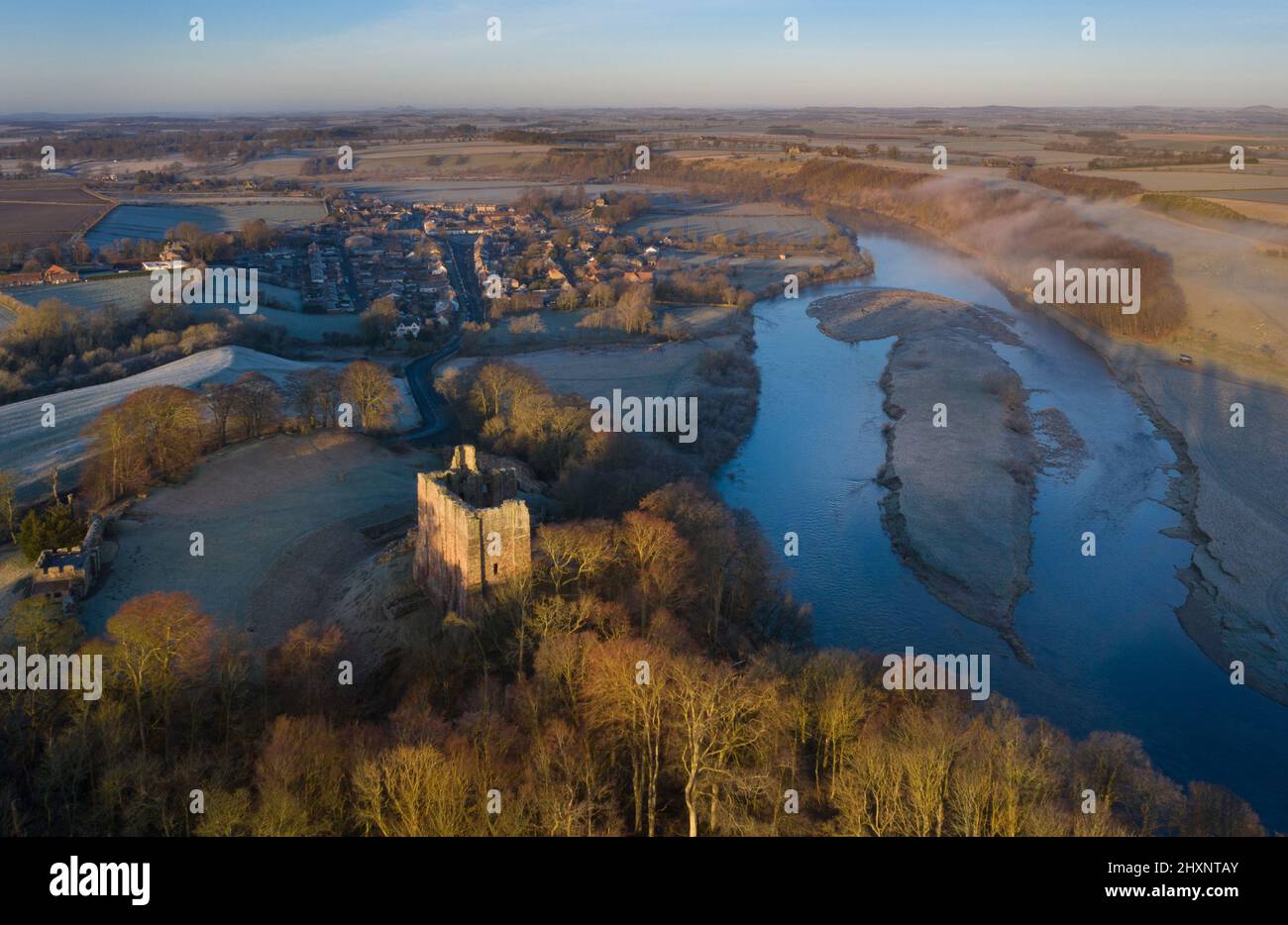 Temprano por la mañana, amanecer helado, vistas de los aviones no tripulados sobre el castillo de Norham, el pueblo de Norham y el río Tweed, Berwick, Northumberland, Inglaterra Foto de stock
