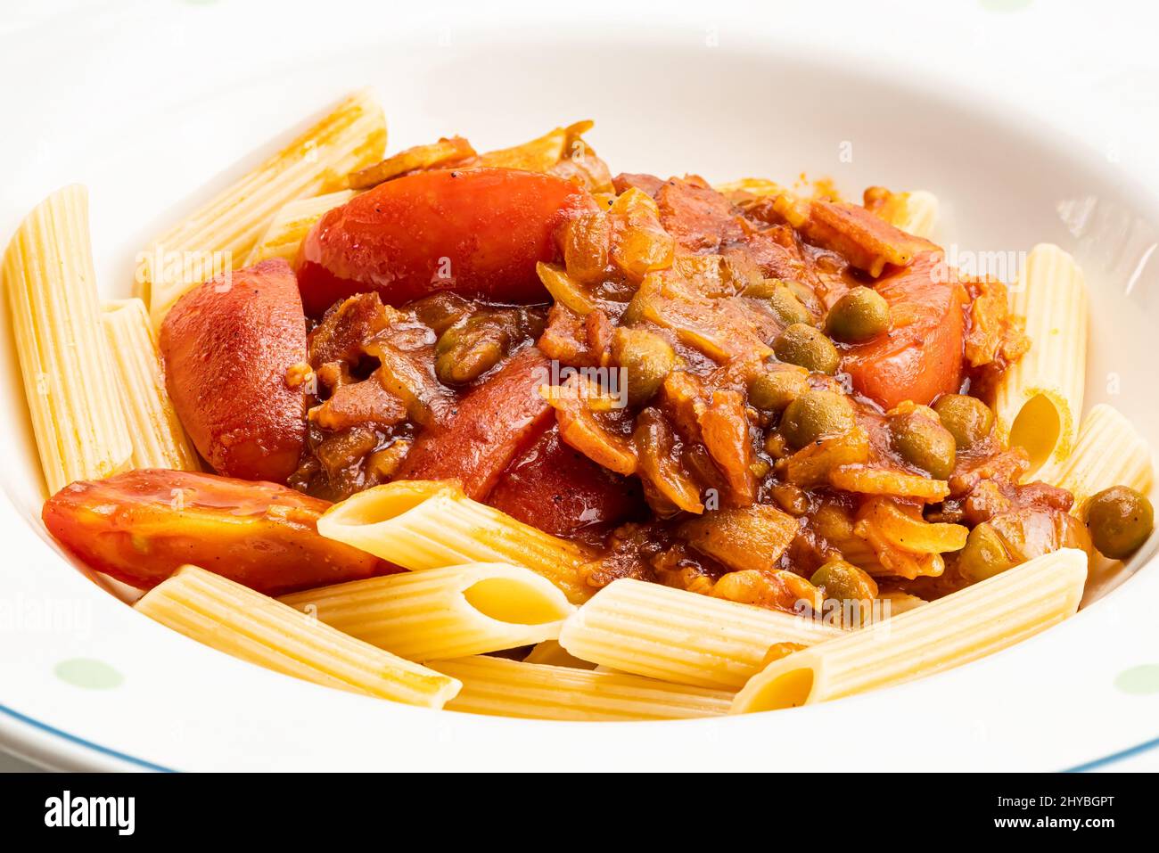 Vista de gran angular de pasta de penne con salsa de tomate con guisante verde, tomate y pollo en plato de cerámica blanca. Foto de stock