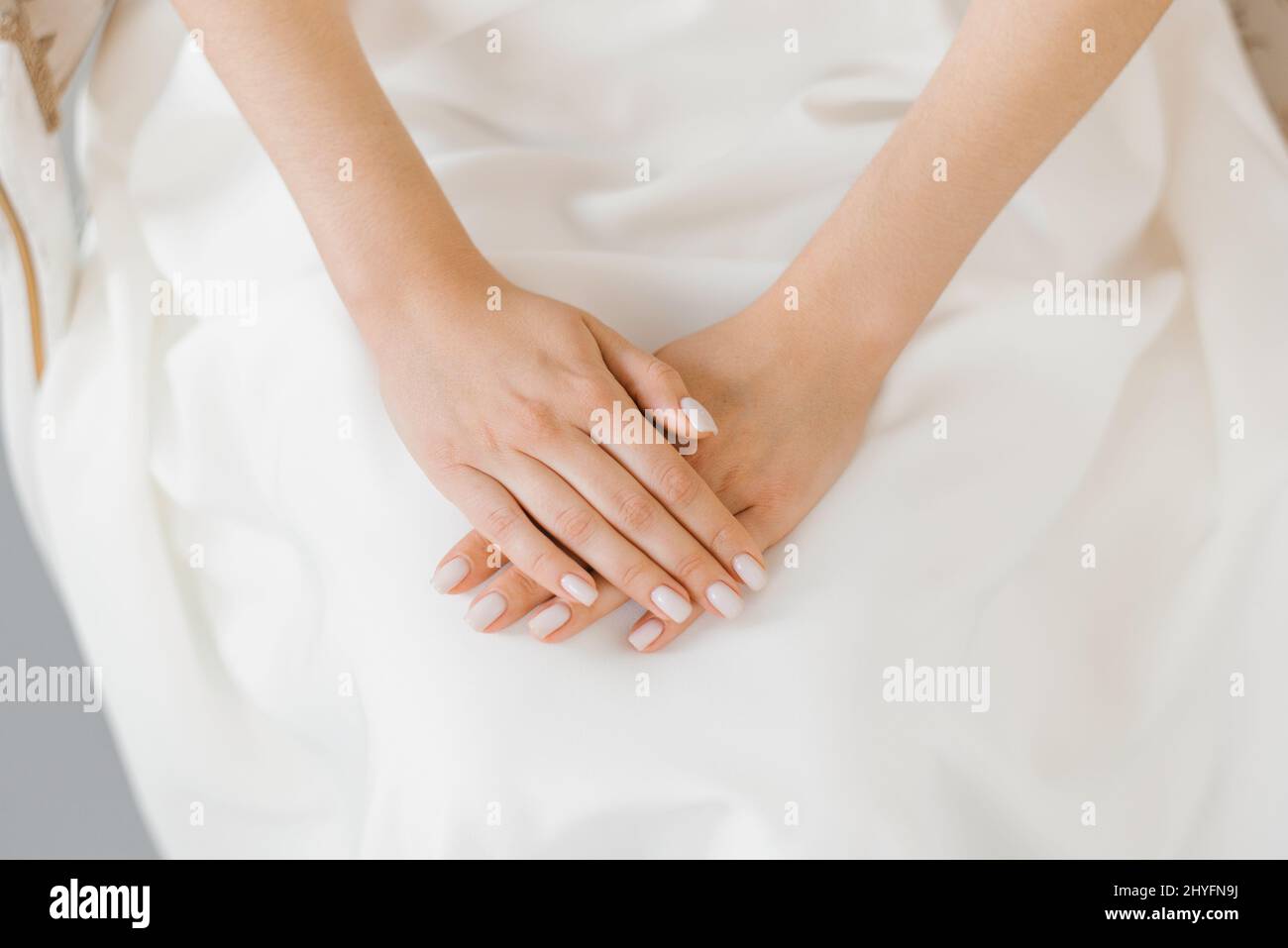 Delicada manicura de la novia, las manos de una mujer joven yacen sobre un vestido blanco de la boda Foto de stock