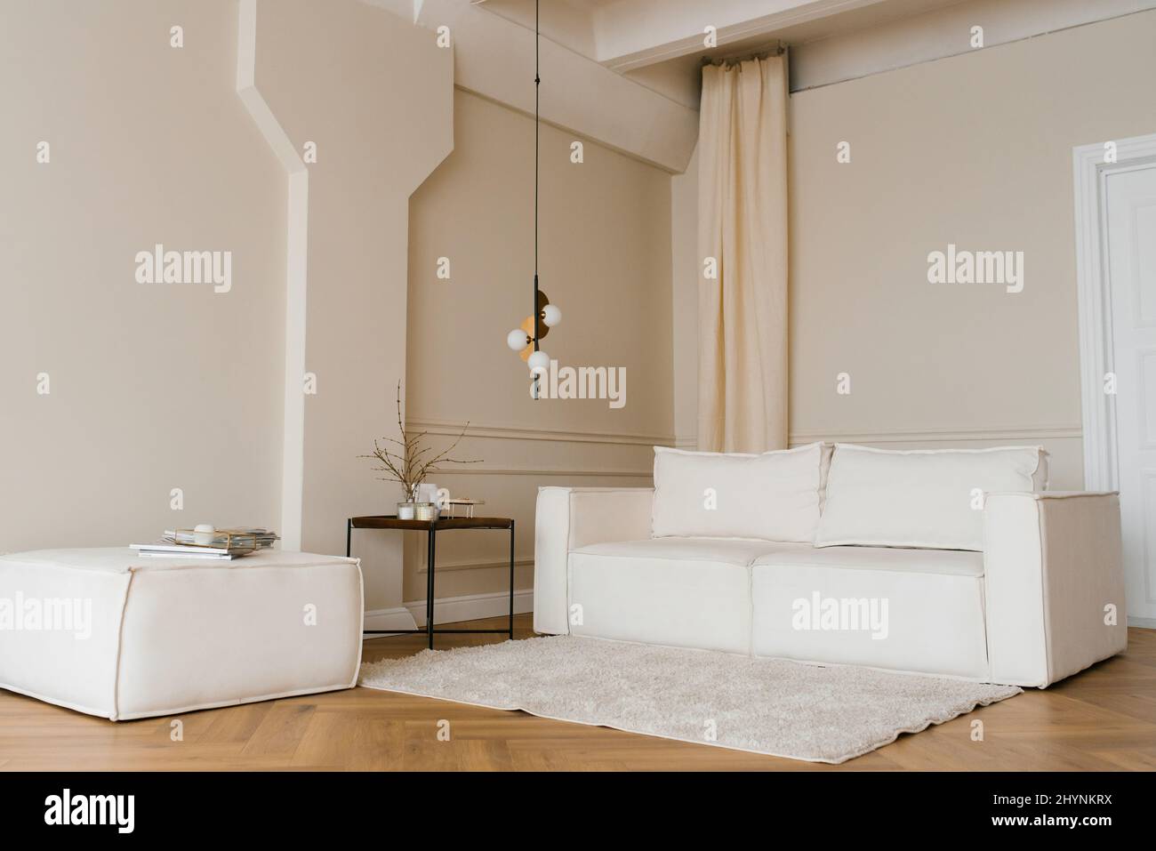 El interior escandinavo tiene un sofá luminoso en el suelo de parqué, una mesa lateral de madera y paredes de color beige Foto de stock