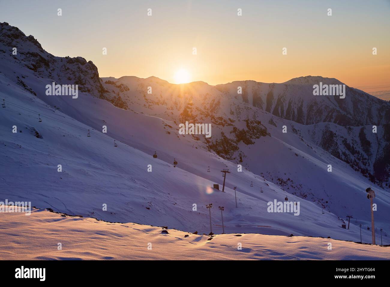 Hermoso paisaje Shymbulak resort montaña nevada vacía pista de esquí y teleférico en la puesta de sol naranja cielo brillar en Almaty, Kazajstán. Foto de stock