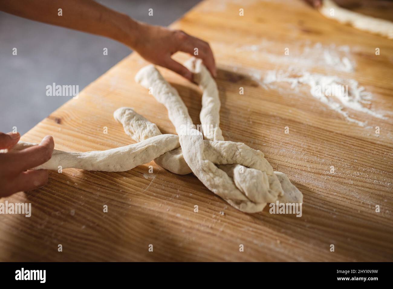 Las manos recortadas de la masa trenzada femenina asiática del panadero del medio adulto mientras que prepara el pan trenzado Foto de stock