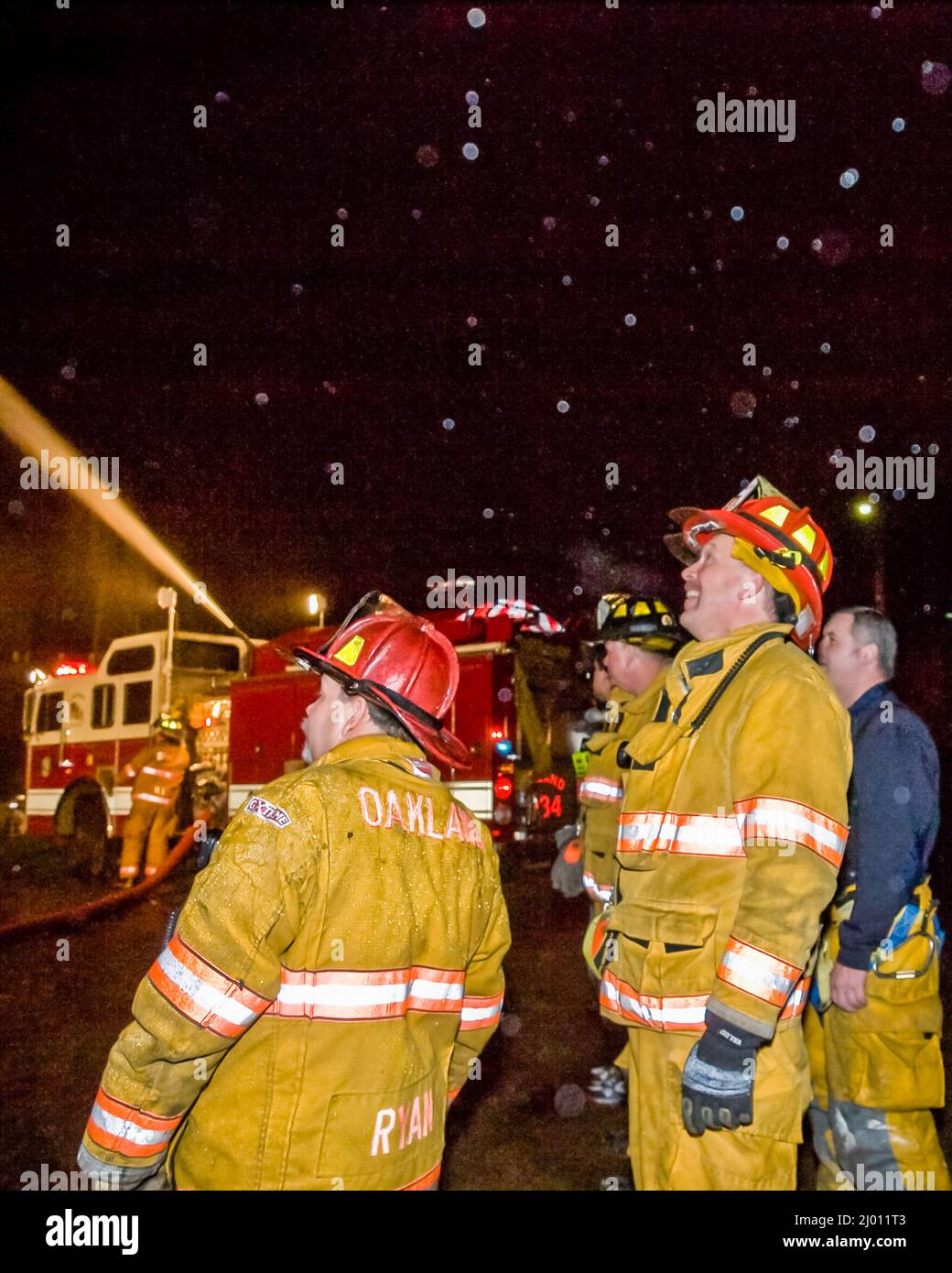 Dos bomberos en acción por la noche con camión y cañón de agua Foto de stock