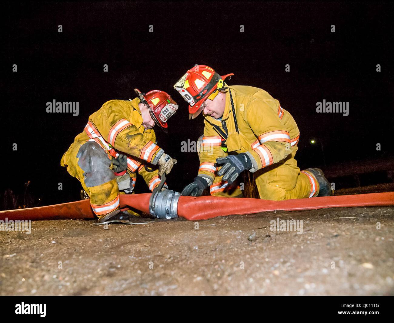 Dos bomberos en acción por la noche con acoplamiento de manguera Foto de stock