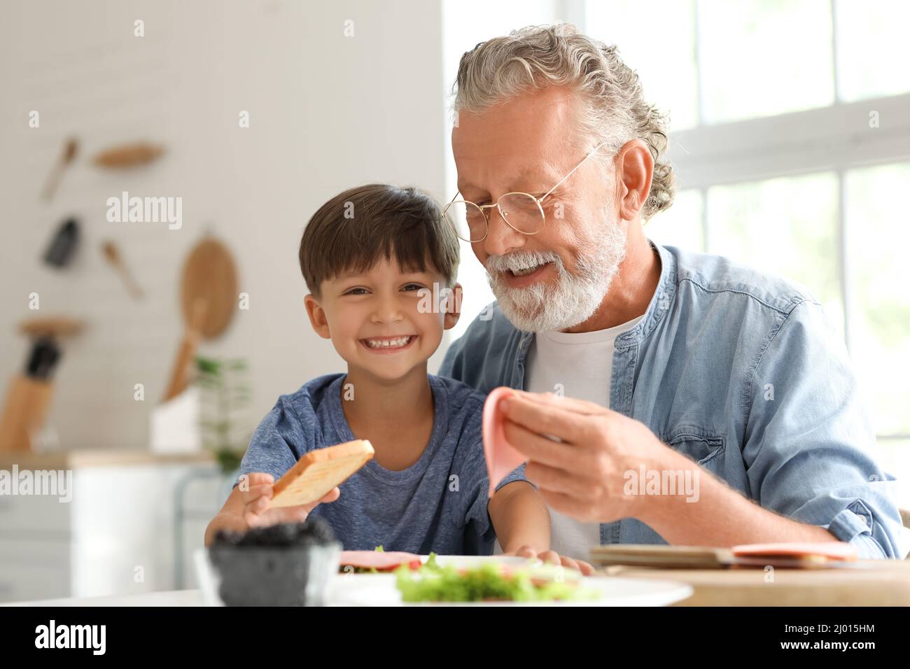 Niño pequeño haciendo un sándwich con su abuelo en la mesa en la cocina Foto de stock