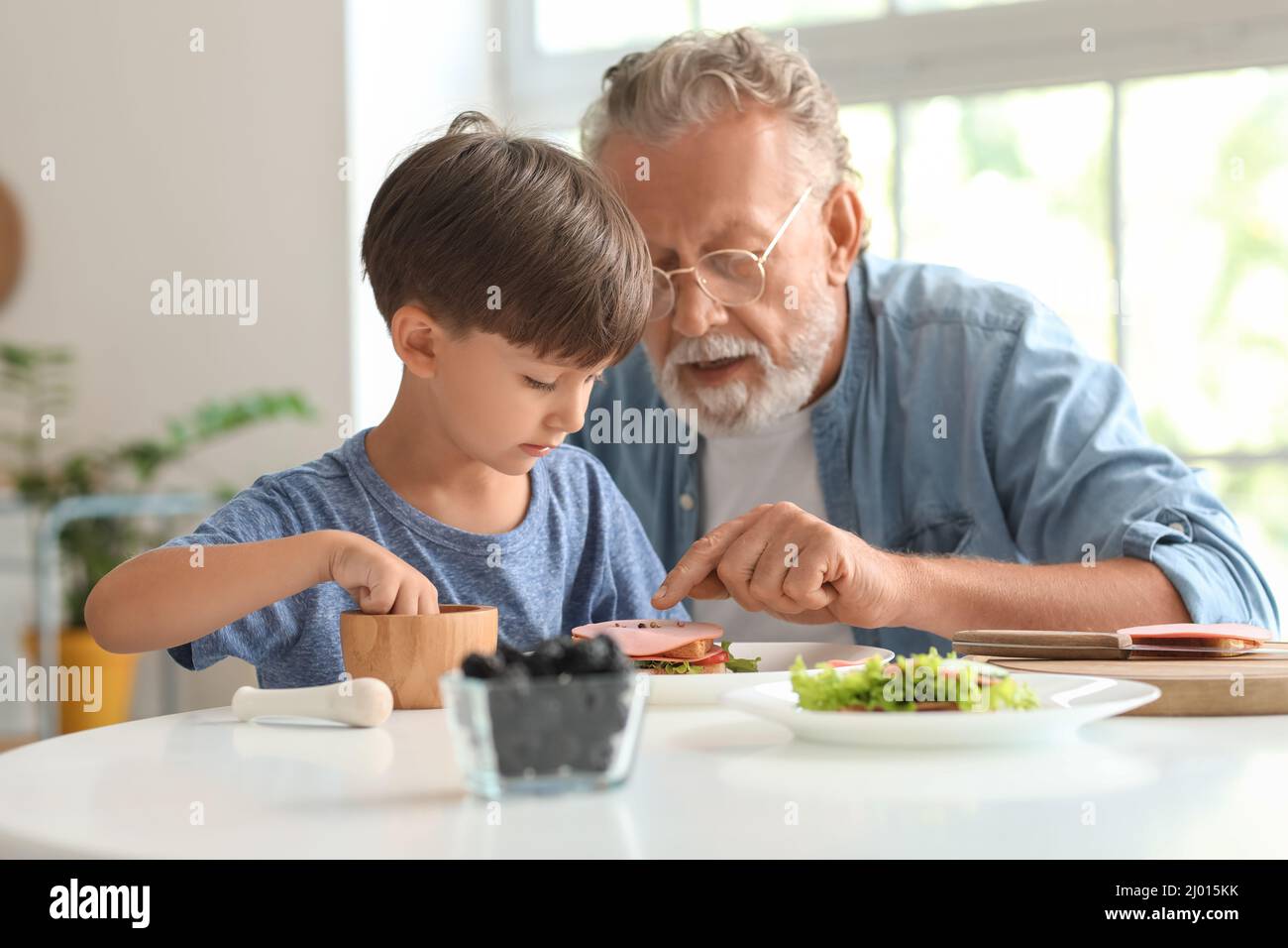 Niño pequeño haciendo un sándwich con su abuelo en la mesa en la cocina Foto de stock