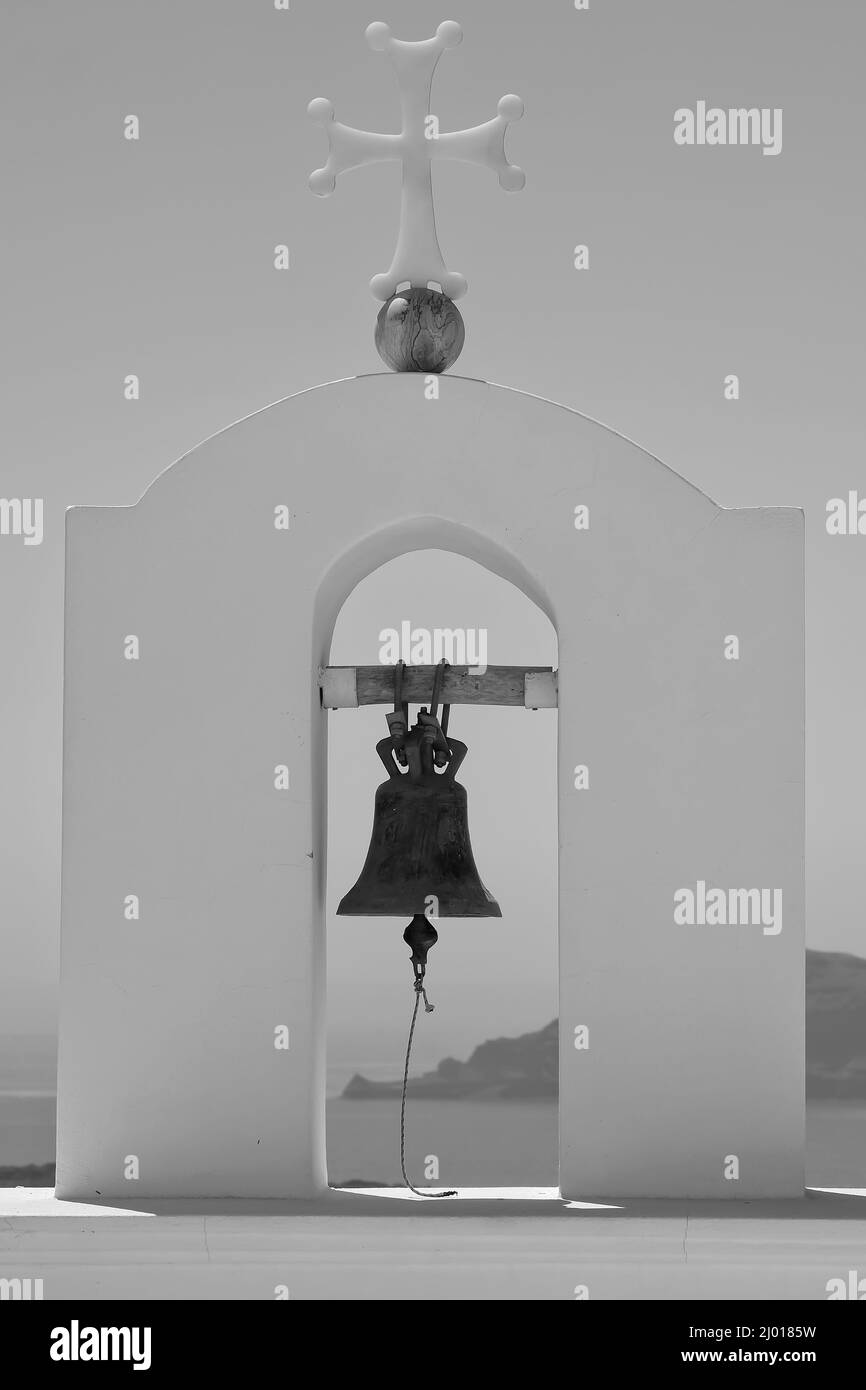 Una campana de la iglesia y una cruz en la parte superior de una iglesia ortodoxa griega y un hermoso cielo azul en Santorini en blanco y negro Foto de stock