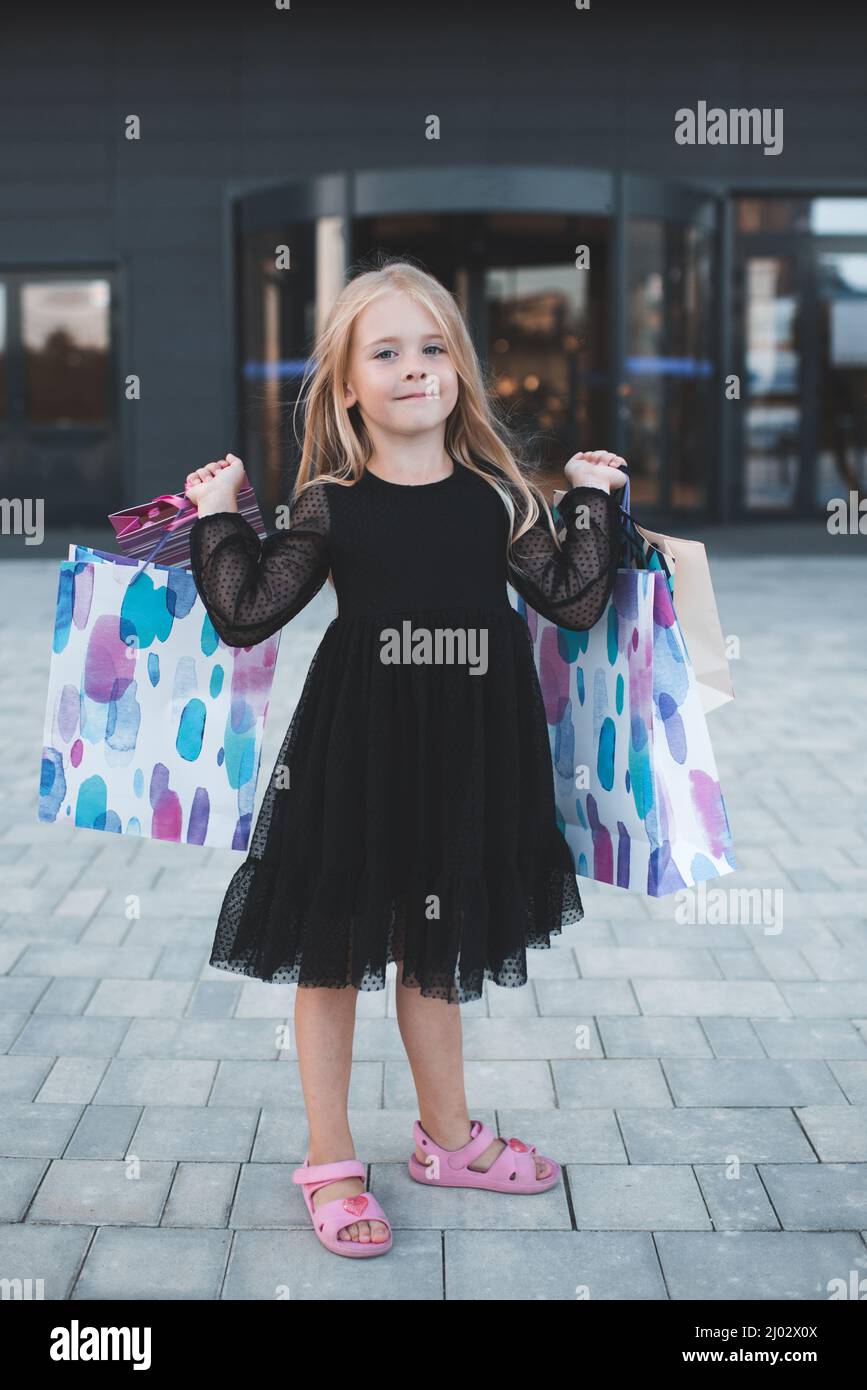 Lindo niño sonriente niña de 4-5 años de edad mantener bolsas de papel de compras en el centro comercial hacer compras. Compra ropa con ventas de temporada. Prepárese para la parte de cumpleaños Foto de stock