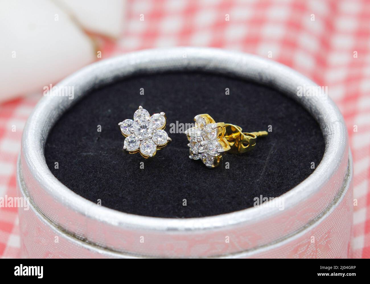 Hermosos pendientes de diamante en forma de flor se muestran en caja de joyas sobre fondo de tela de cuadros rojos Foto de stock