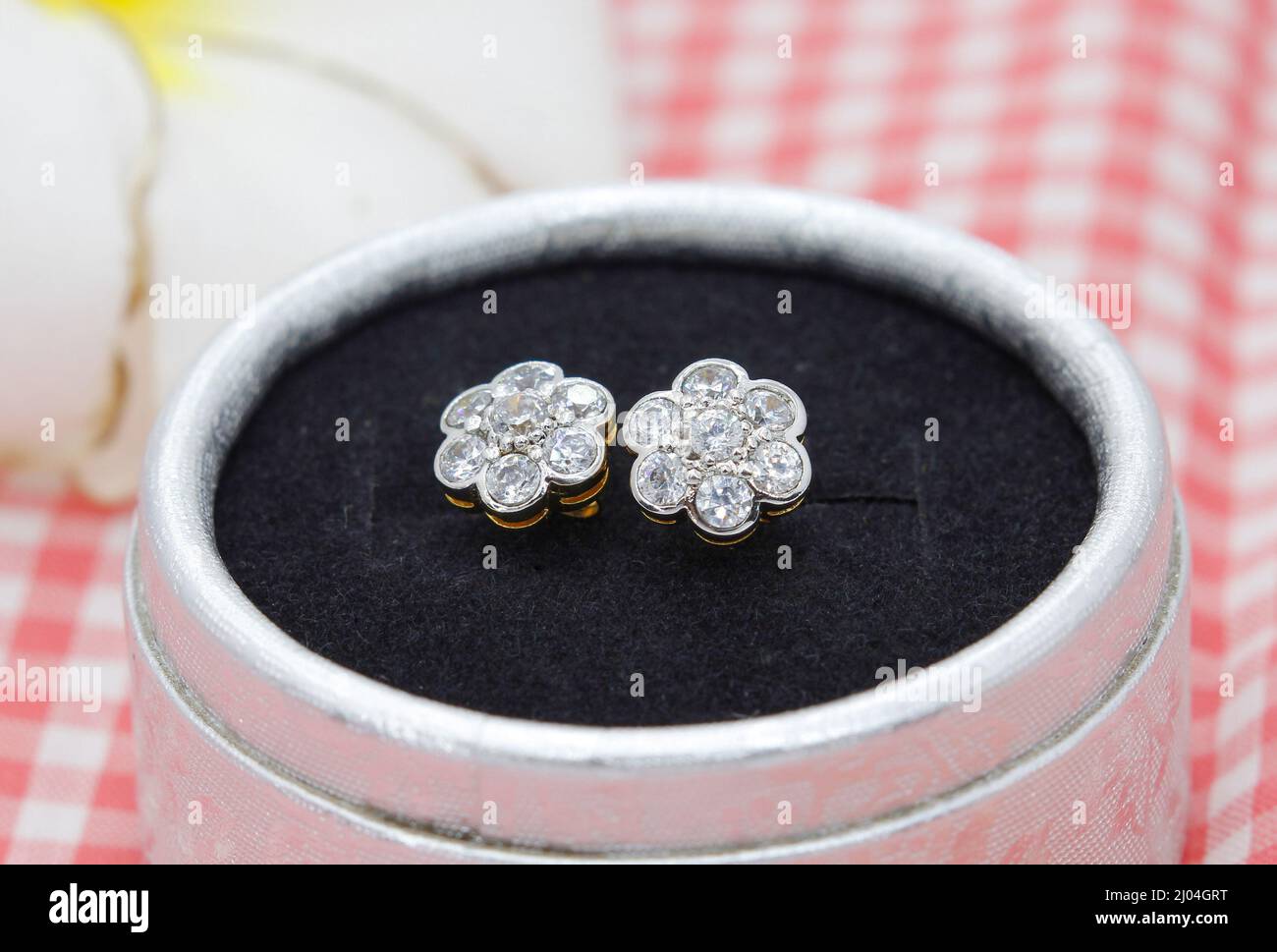 Hermosos pendientes de diamante en forma de flor se muestran en caja de joyas sobre fondo de tela a cuadros Foto de stock
