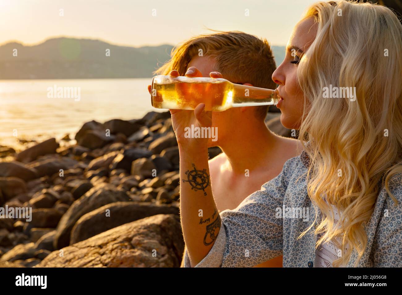 Mujer joven bebiendo cerveza por novio en la playa Foto de stock