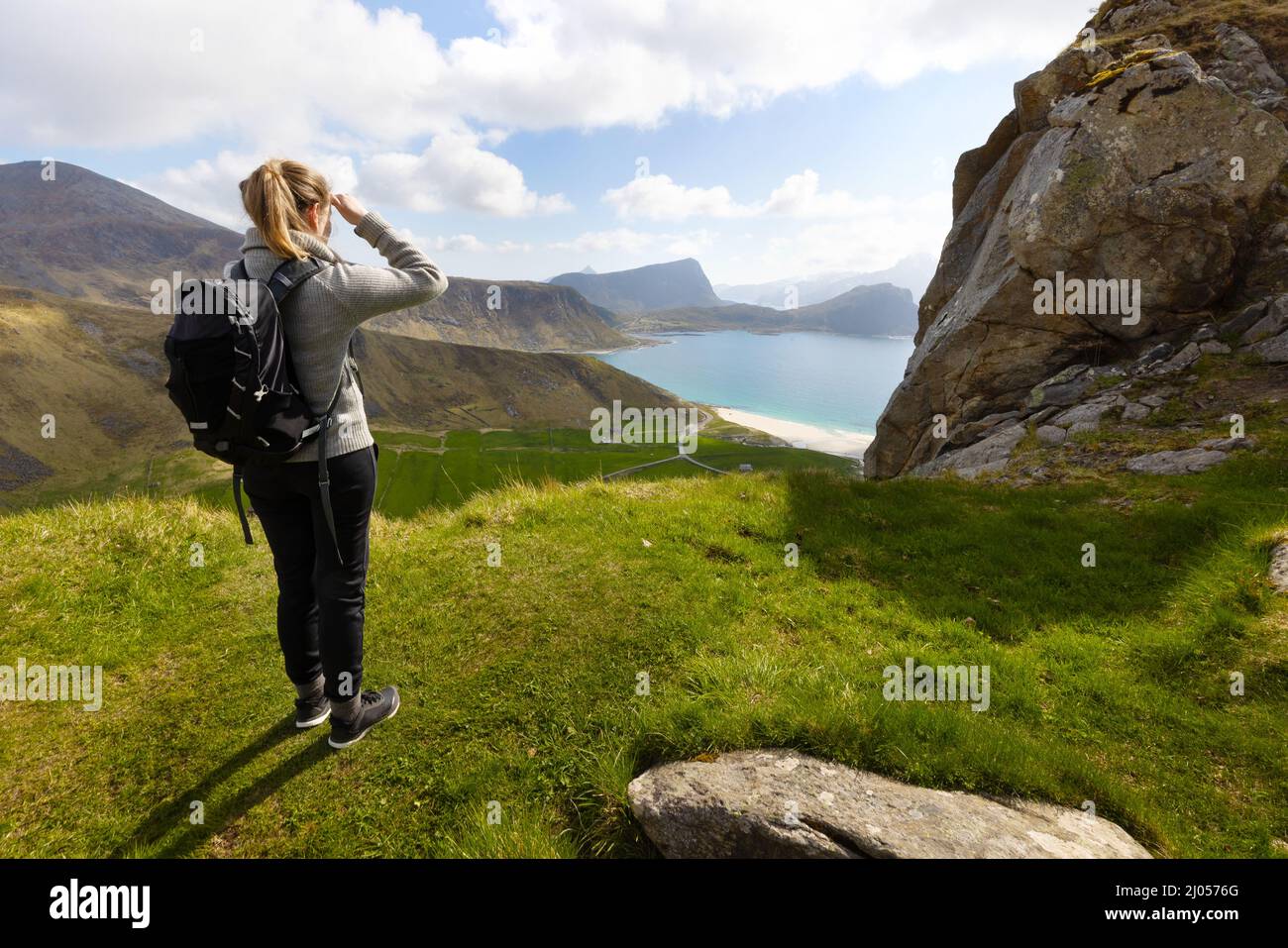 Mujer haciendo senderismo en las altas montañas y mirando la playa Haukland en la isla Vestvagoy en Lofoten, Noruega Foto de stock