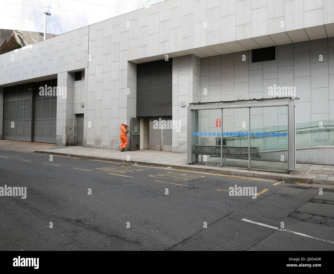 Trabajador en ropa de alta visibilidad PPE toma un descanso cerca de una parada de autobús en la calle de la ciudad. Birmingham Reino Unido Foto de stock