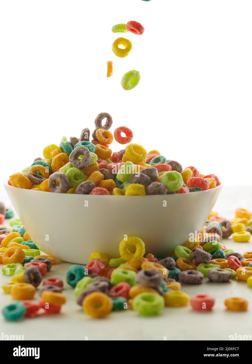 Anillos crujientes de cereales multicolor en un recipiente y cerca de él  sobre un fondo blanco. Primer plano. Desayunos rápidos de cereales,  nutrientes, vitaminas, estilo de vida saludable Fotografía de stock -