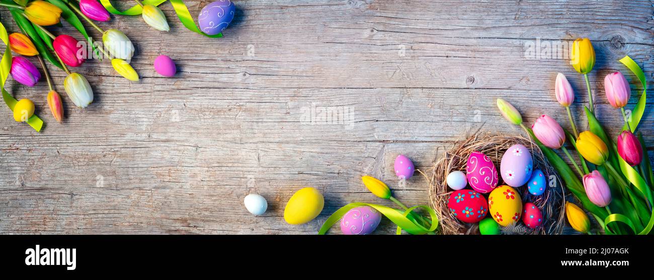 Huevos de Pascua - Decoración pintada en Nido con Tulipanes sobre Plank de madera natural Foto de stock