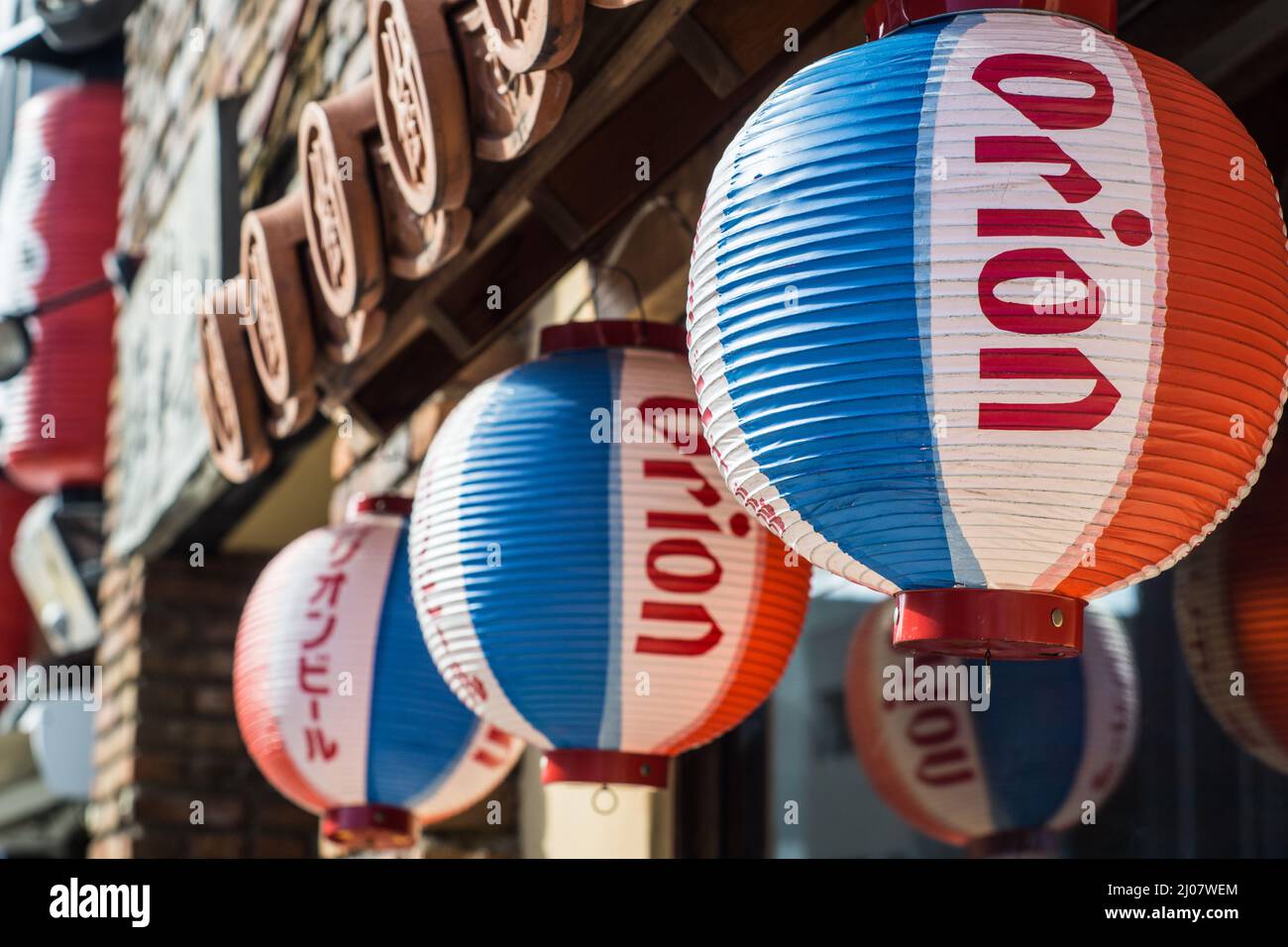 Primer plano de linternas japonesas de papel colgante rojo, azul y blanco que promueven la cerveza Orión fuera de un restaurante de Okinawa en Nara, Japón Foto de stock