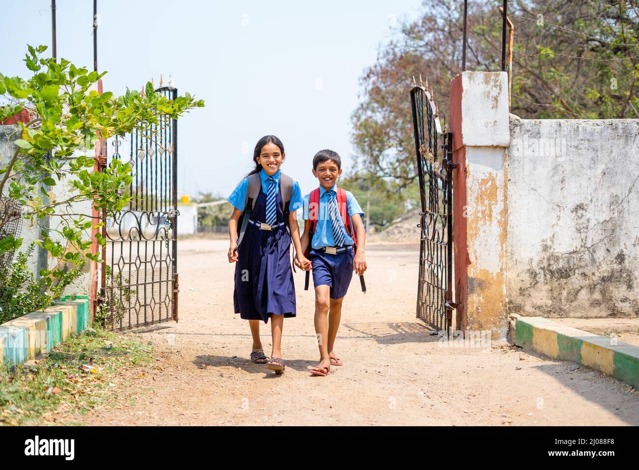 Feliz adolescente hermanos niños en uniforme que entran a la escuela desde GATE - concepto de educación, de vuelta a la escuela y el aprendizaje. Foto de stock