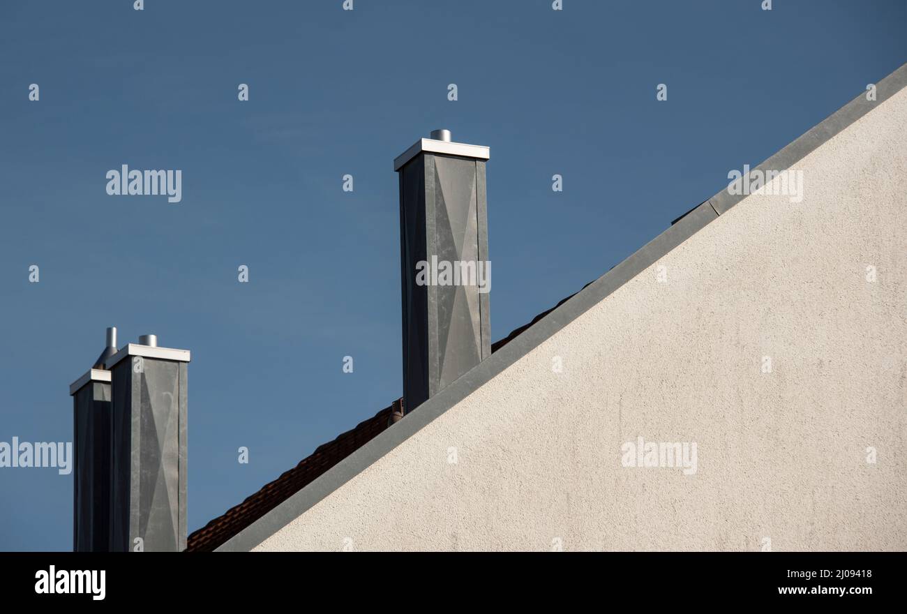 las chimeneas cubiertas de metal en la azotea de una casa con una fachada enyesada Foto de stock