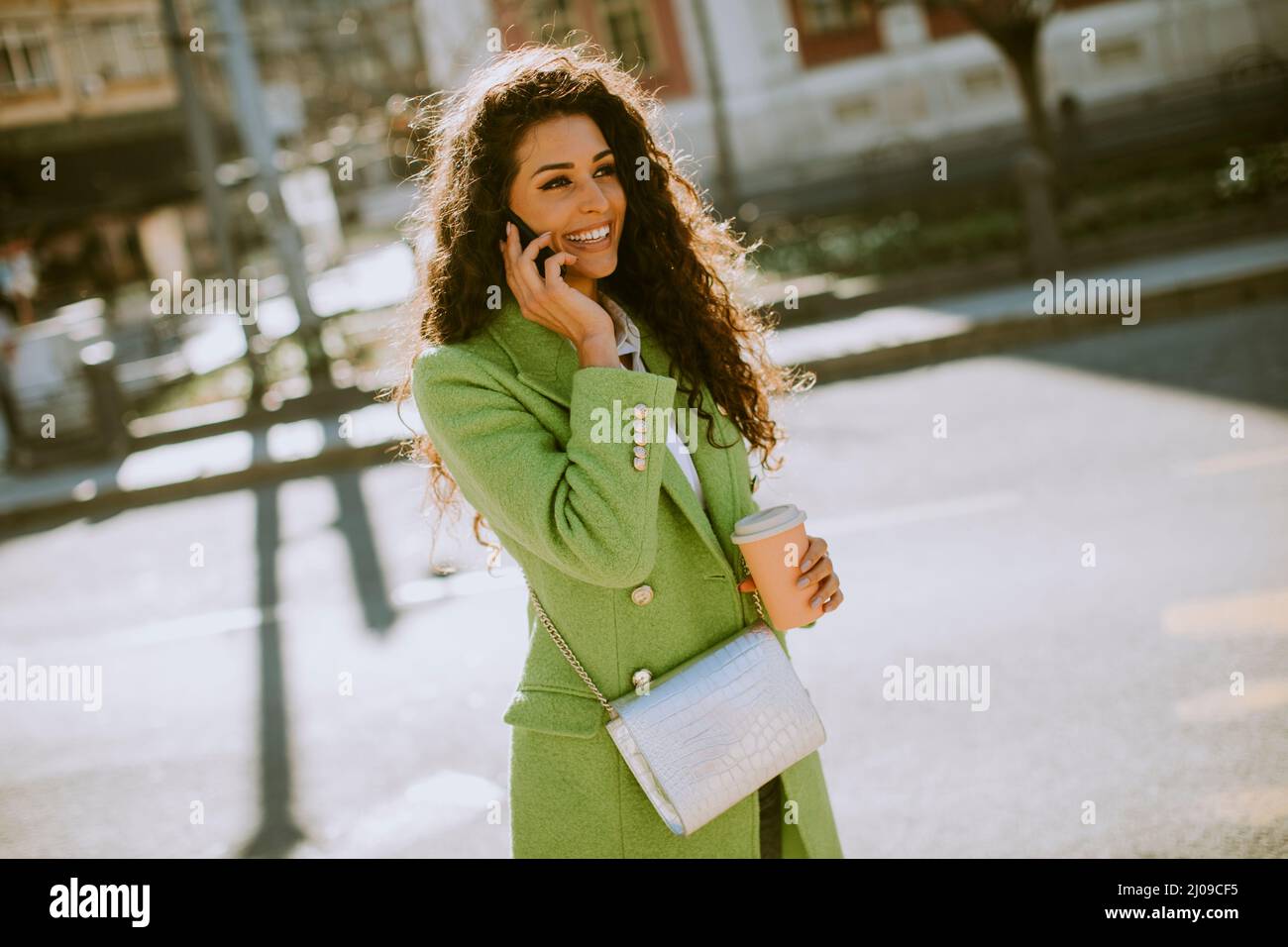 Una mujer joven con un smartphone en la calle y tomando café para llevar Foto de stock
