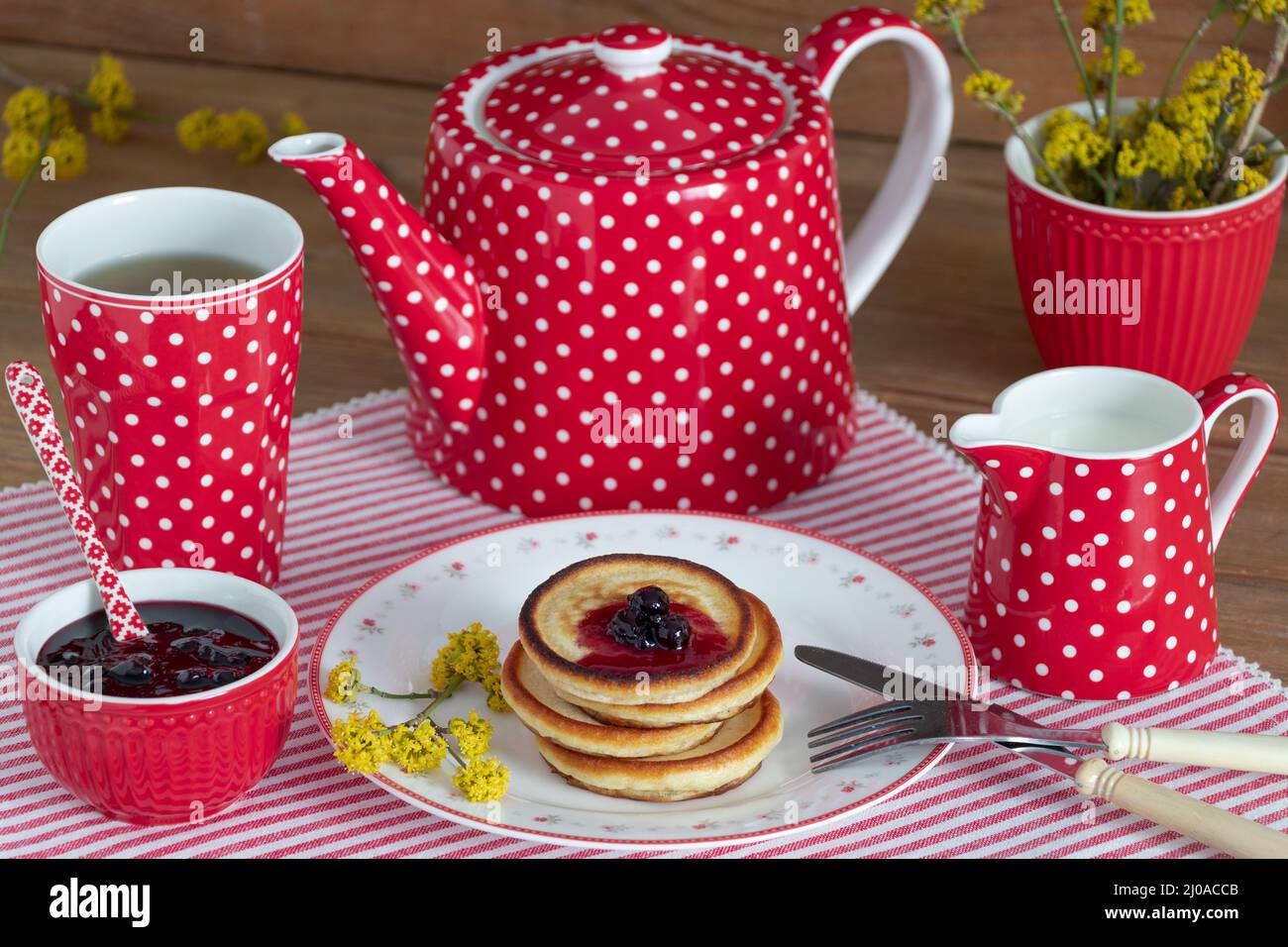 panqueques con mermelada de grosella en el plato y set de té rojo Foto de stock