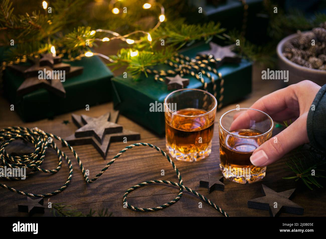 Mano femenina sosteniendo un vaso de whisky o bourbon con decoración navideña sobre fondo oscuro. Año Nuevo, Navidad y vacaciones de invierno whiskey humor concip Foto de stock