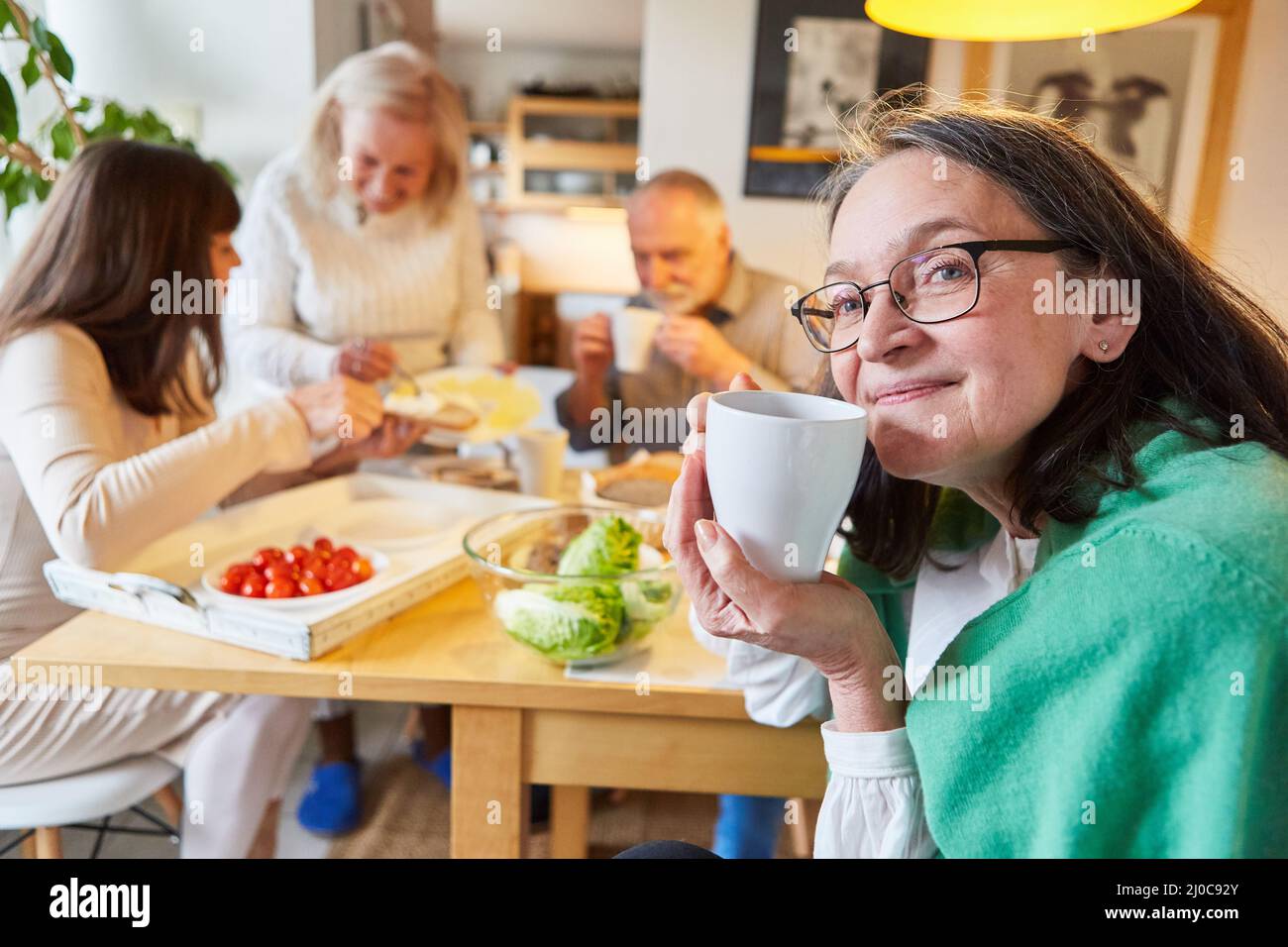 Una mujer mayor y un grupo de amigos que tienen brunch y una taza de café juntos en la cocina Foto de stock