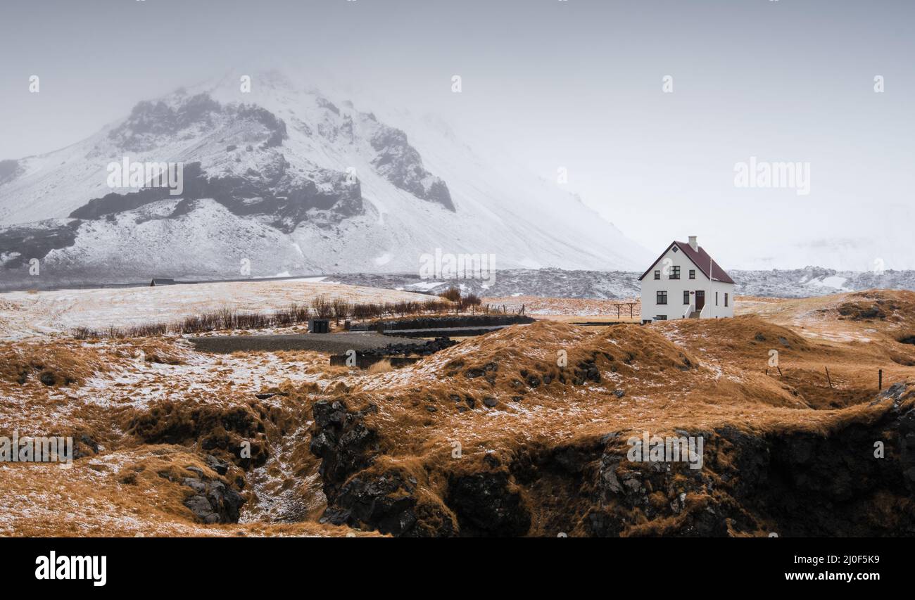 Casa solitaria en el pequeño pueblo pesquero de Arnarstapi y acantilado de montaña cubierto de nieve en SnÃ¦f Foto de stock
