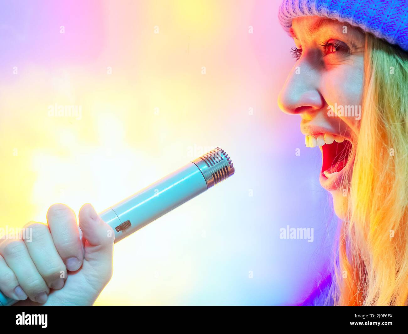Chica canta en un antiguo micrófono de estudio soviético sobre fondo multicolor Foto de stock