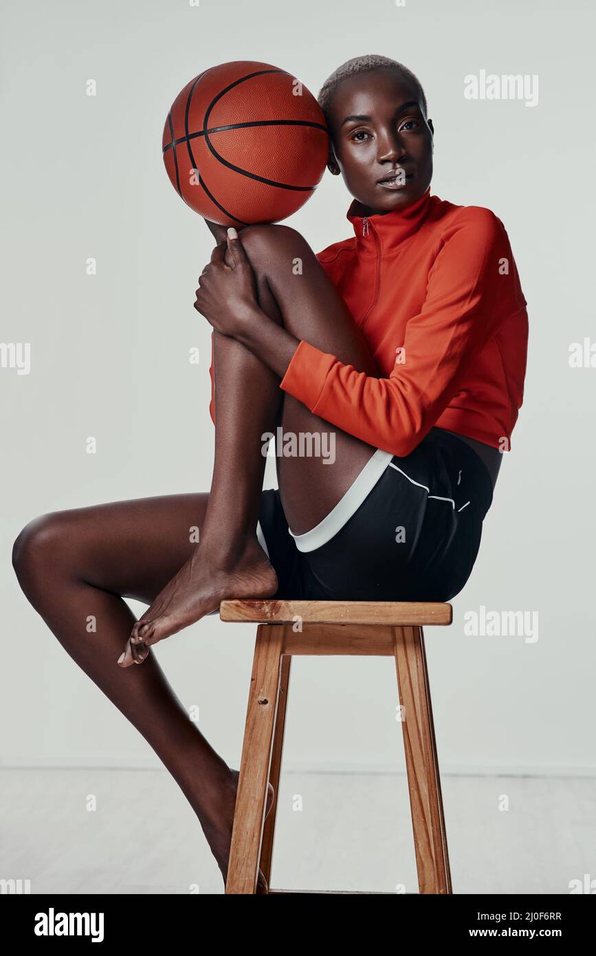 Joven Mujer afroamericana en vestimenta deportiva y tacones altos sentados  en las escaleras de madera en la cancha de deportes y sosteniendo una  pelota de baloncesto Fotografía de stock - Alamy
