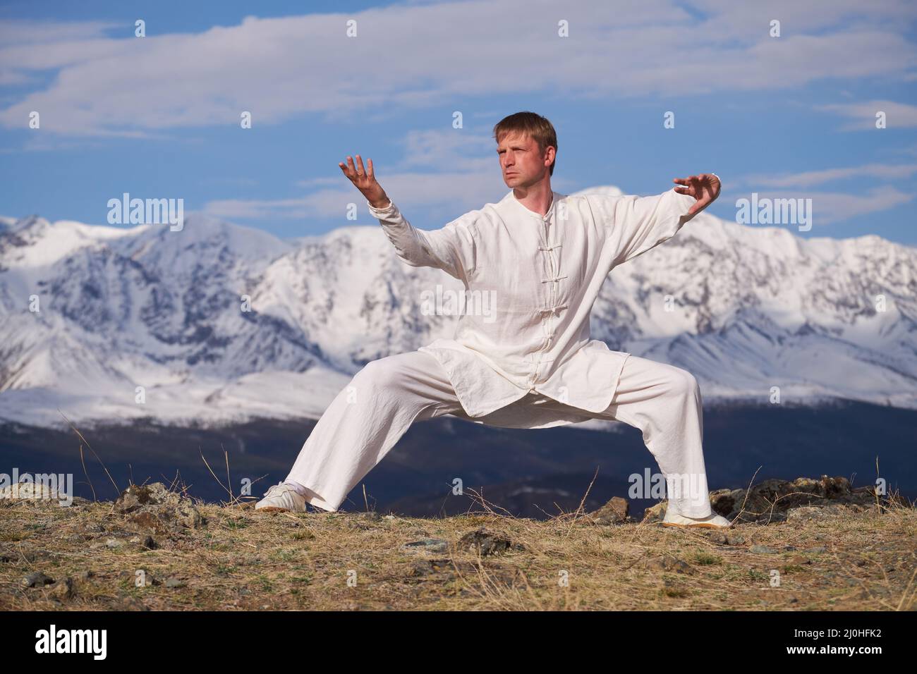 Wushu maestro en un deporte blanco uniforme de entrenamiento kungfu en la naturaleza en el fondo de las montañas nevadas. Foto de stock