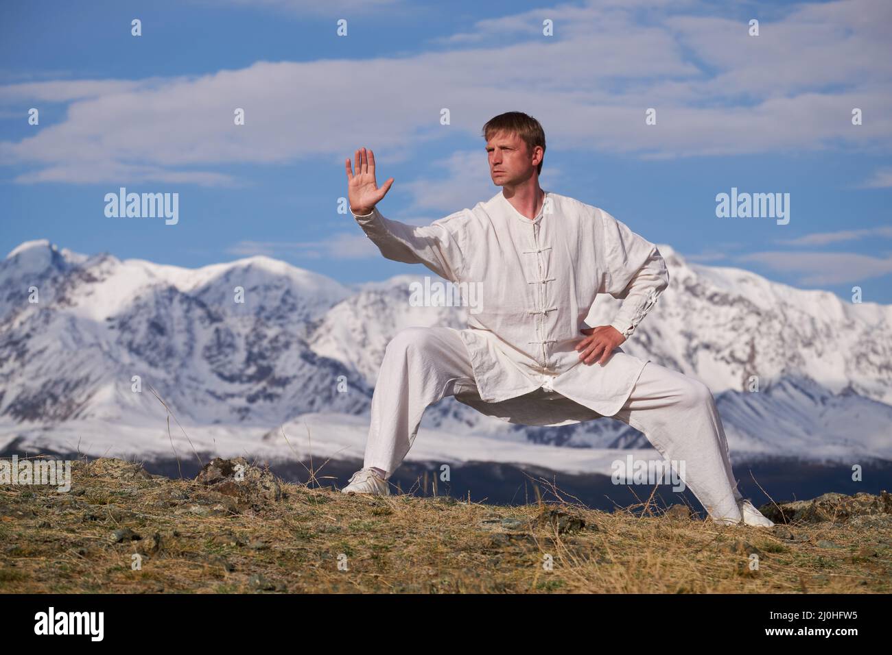 Wushu maestro en un deporte blanco uniforme de entrenamiento kungfu en la naturaleza en el fondo de las montañas nevadas. Foto de stock