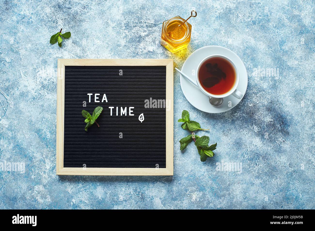 Hora del té. Pizarra negra con texto sobre mesa azul con vaso de té con hojas de menta Foto de stock