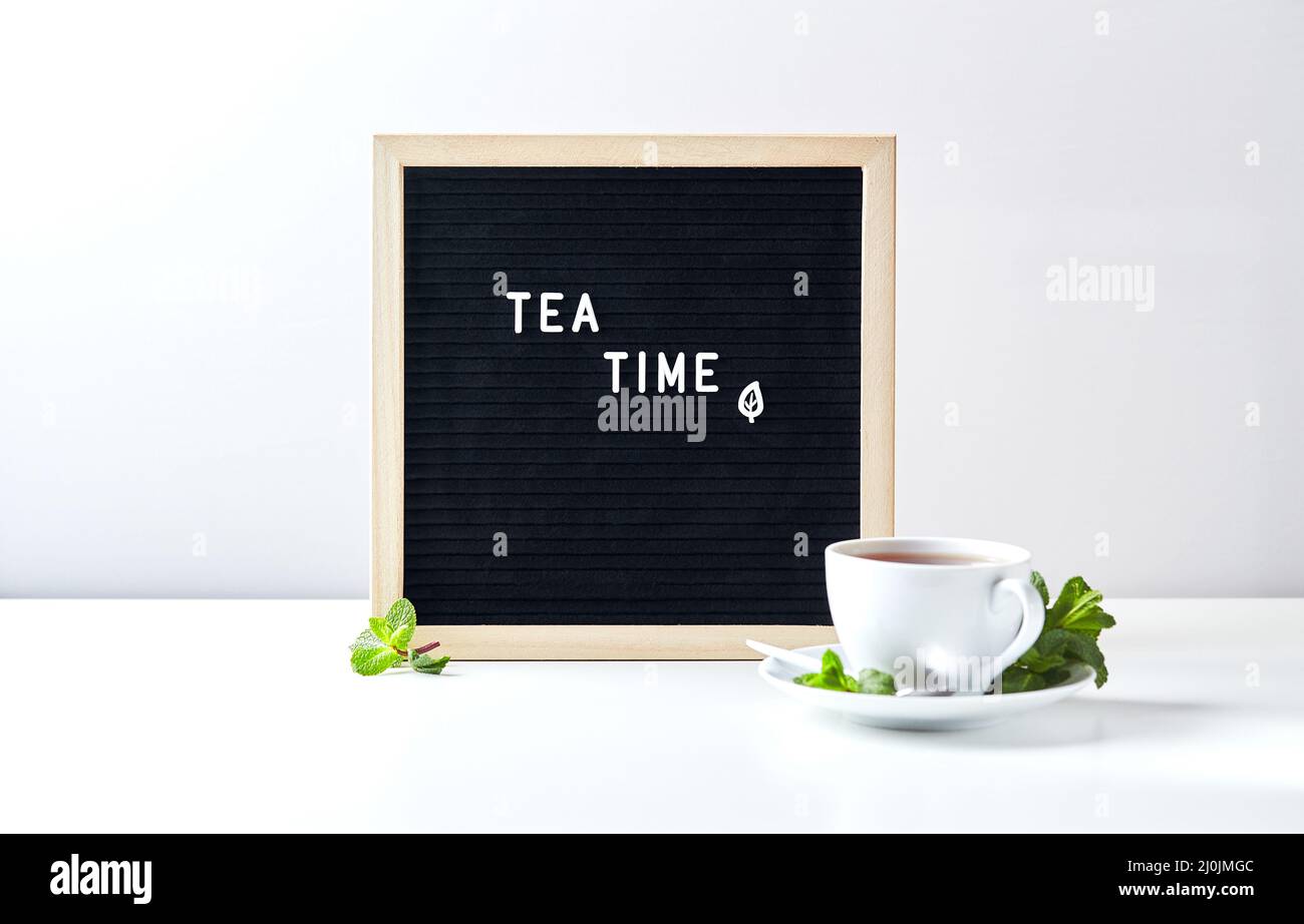 Hora del té. Pizarra negra con texto sobre mesa con vaso de té con hojas de menta Foto de stock