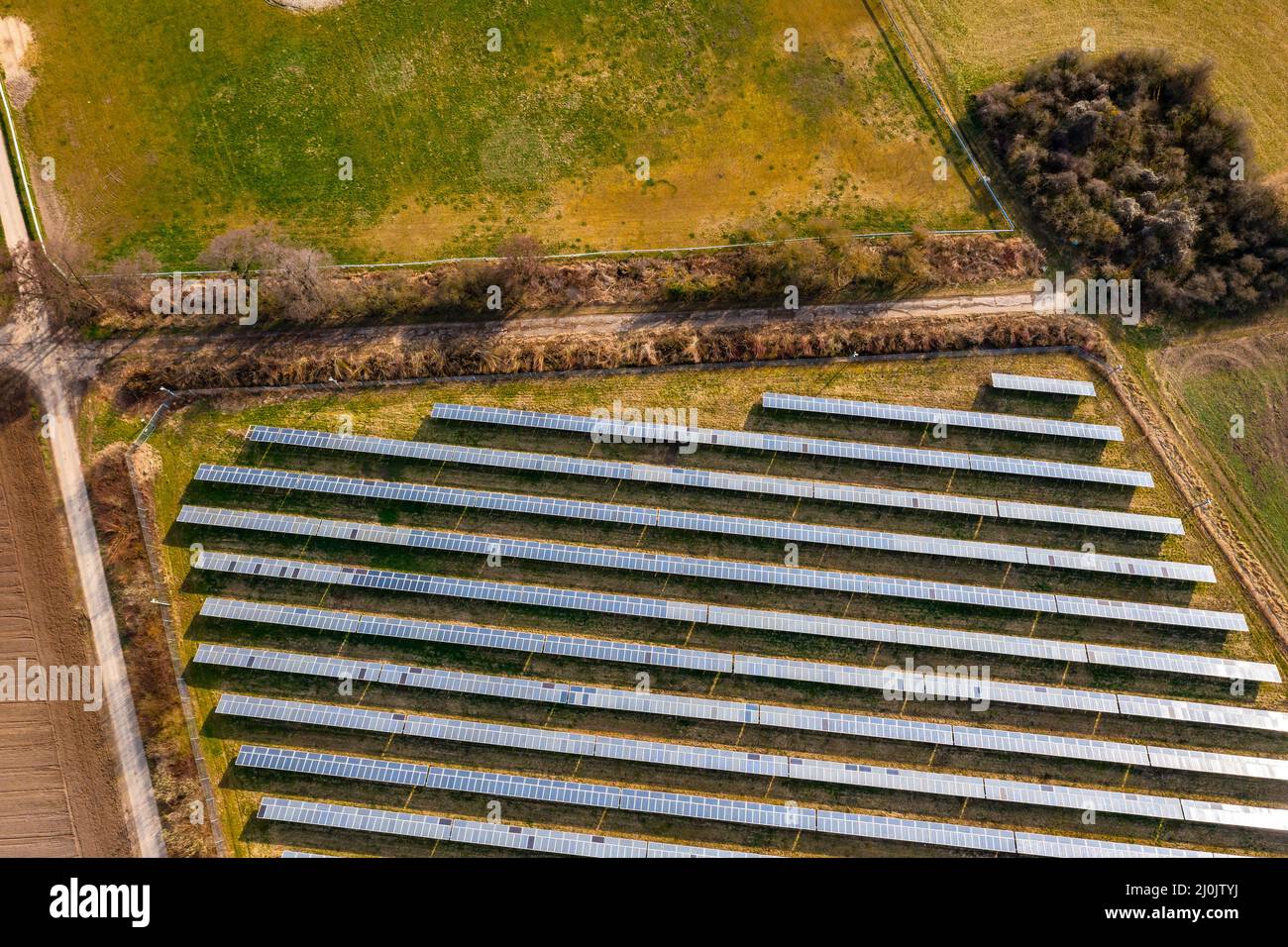 Un sistema solar fotovoltaico montado en tierra con paneles solares, arbustos, pistas agrícolas y prados en Alemania desde una vista de drone Foto de stock