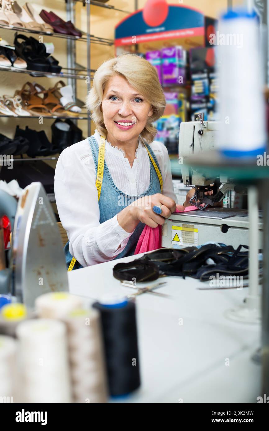 alegre mujer de mediana edad sastre con máquina de coser Foto de stock