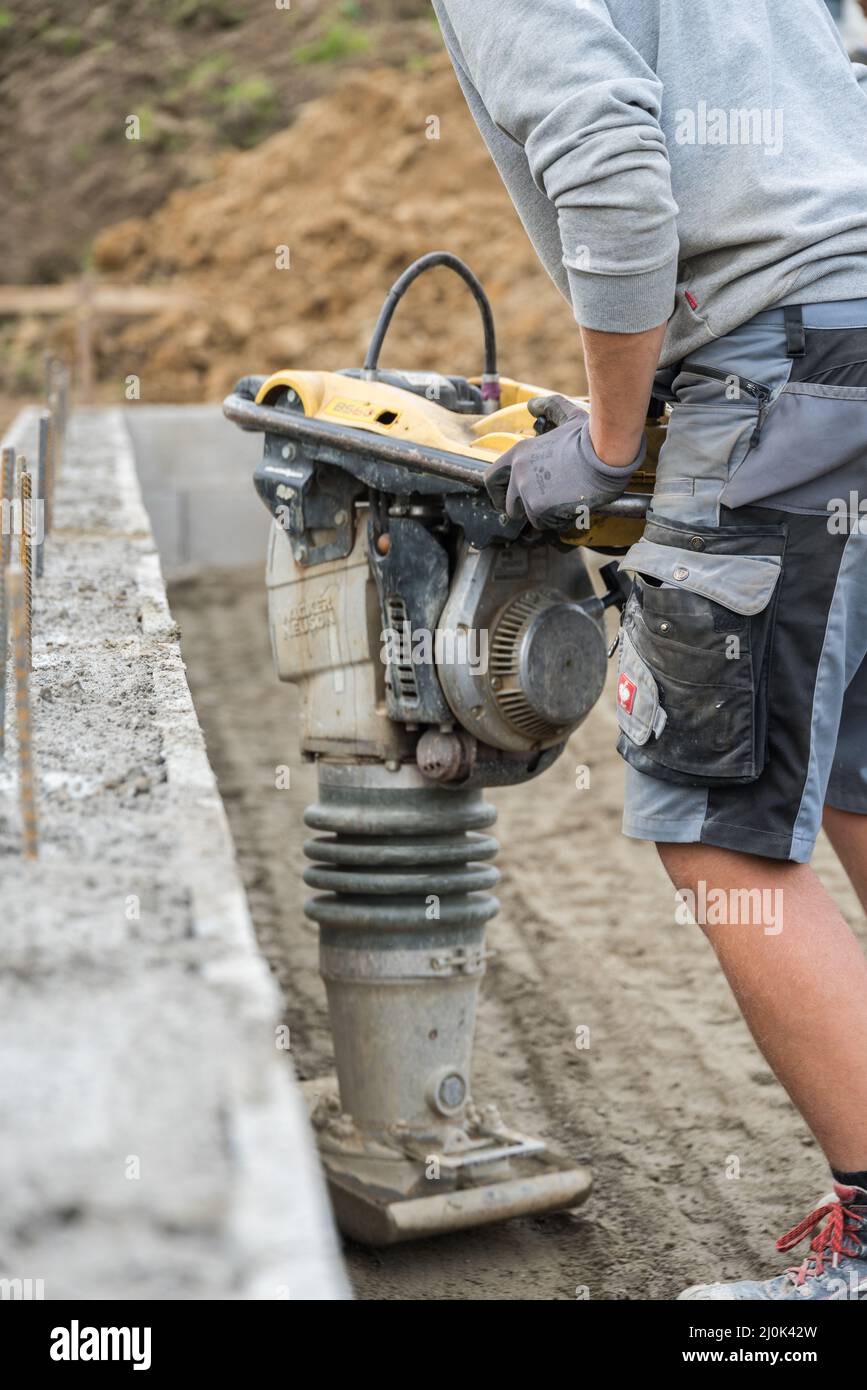 El trabajador de la construcción compacta el suelo con la ramera - cerca del comercio de la construcción Foto de stock