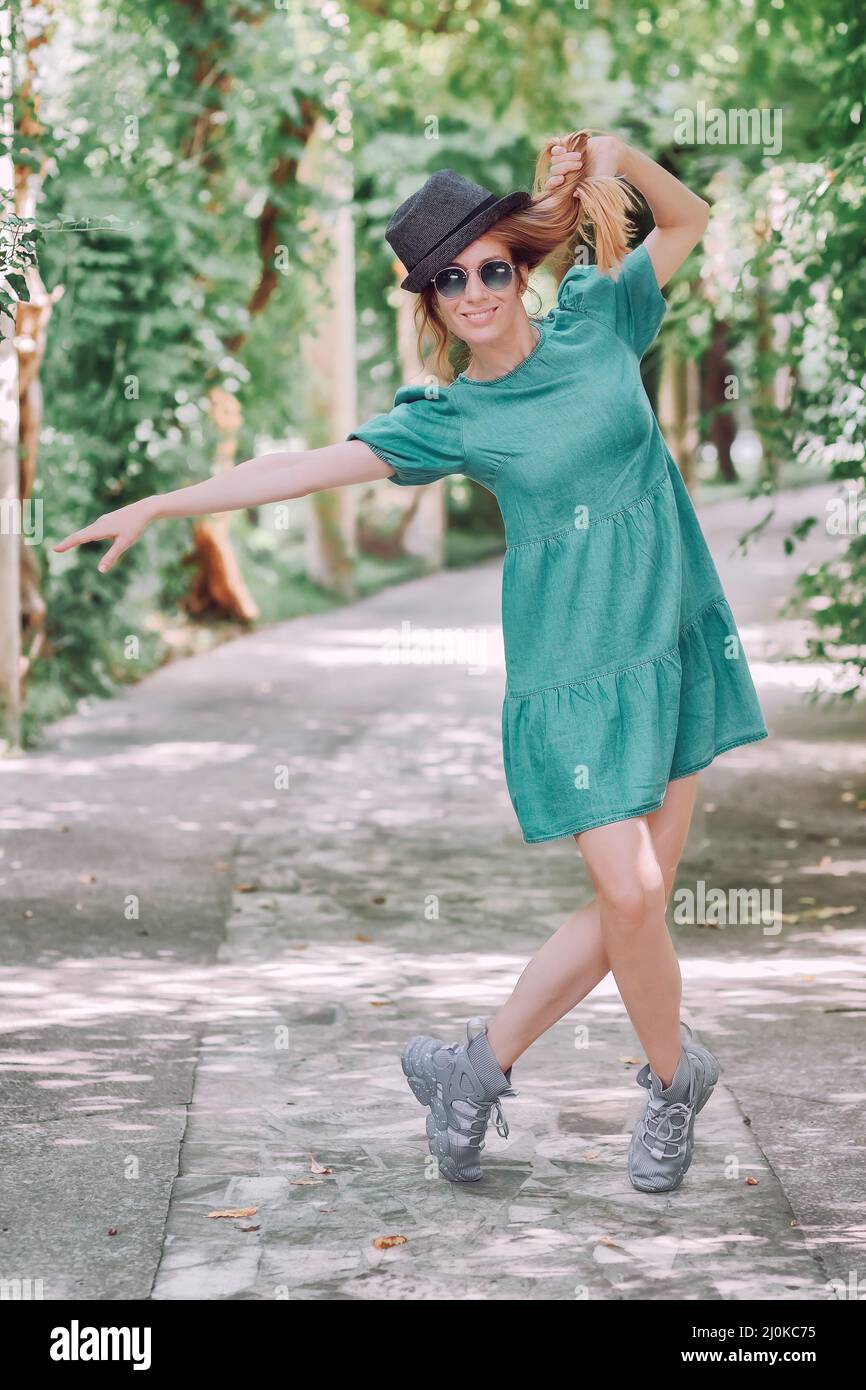 Chica alegre posando en el parque en el callejón de pie en los dedos de los pies y sujetándose por el pelo Foto de stock