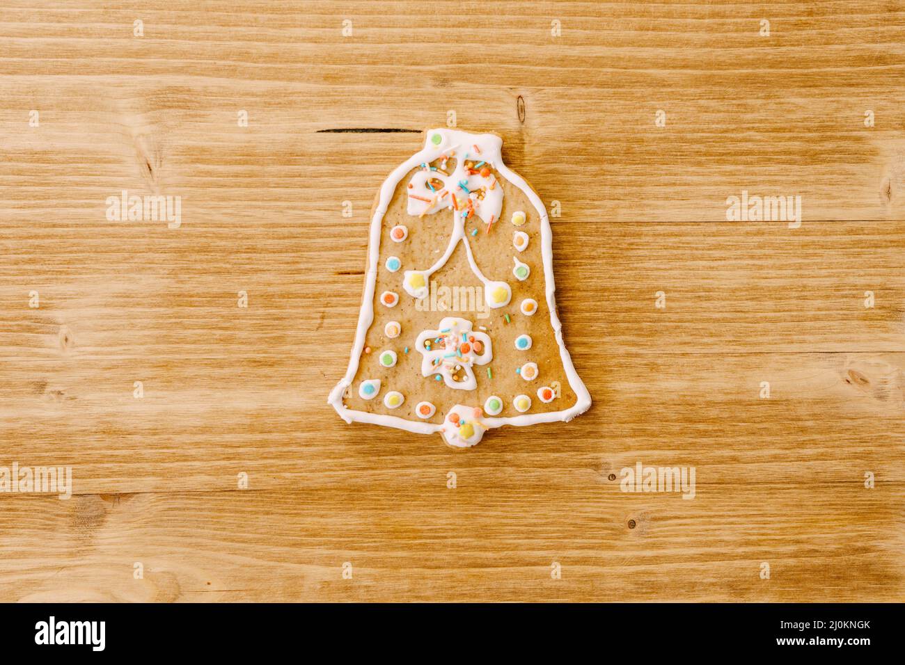 Pan de jengibre en forma de campana, decorado con hielo y rociado, sobre un fondo de textura de madera clara. Foto de stock