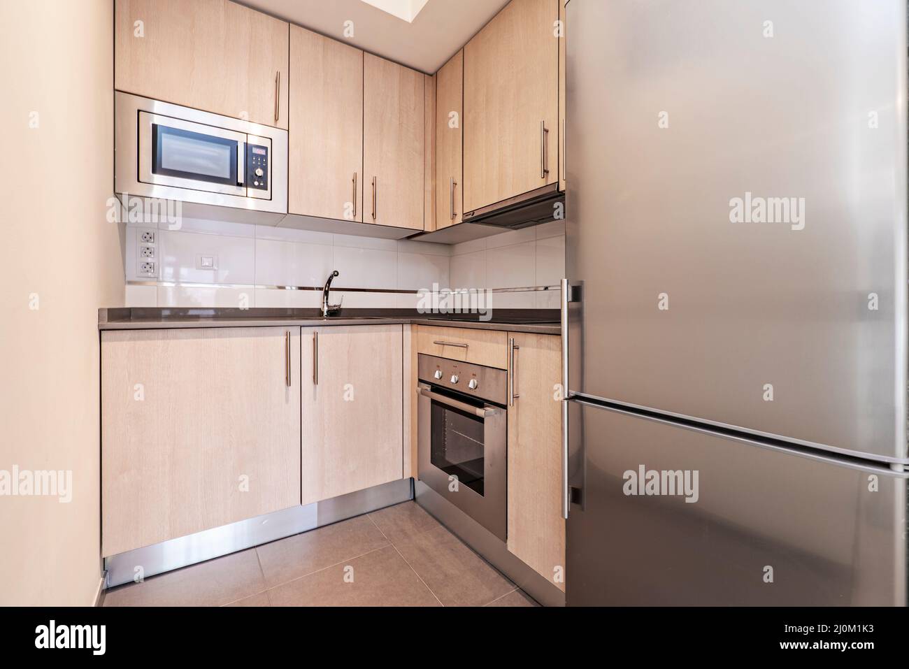 cocina abierta equipada con armarios de color madera, encimeras de piedra  gris y electrodomésticos de acero inoxidable con microondas y horno de  convección Fotografía de stock - Alamy