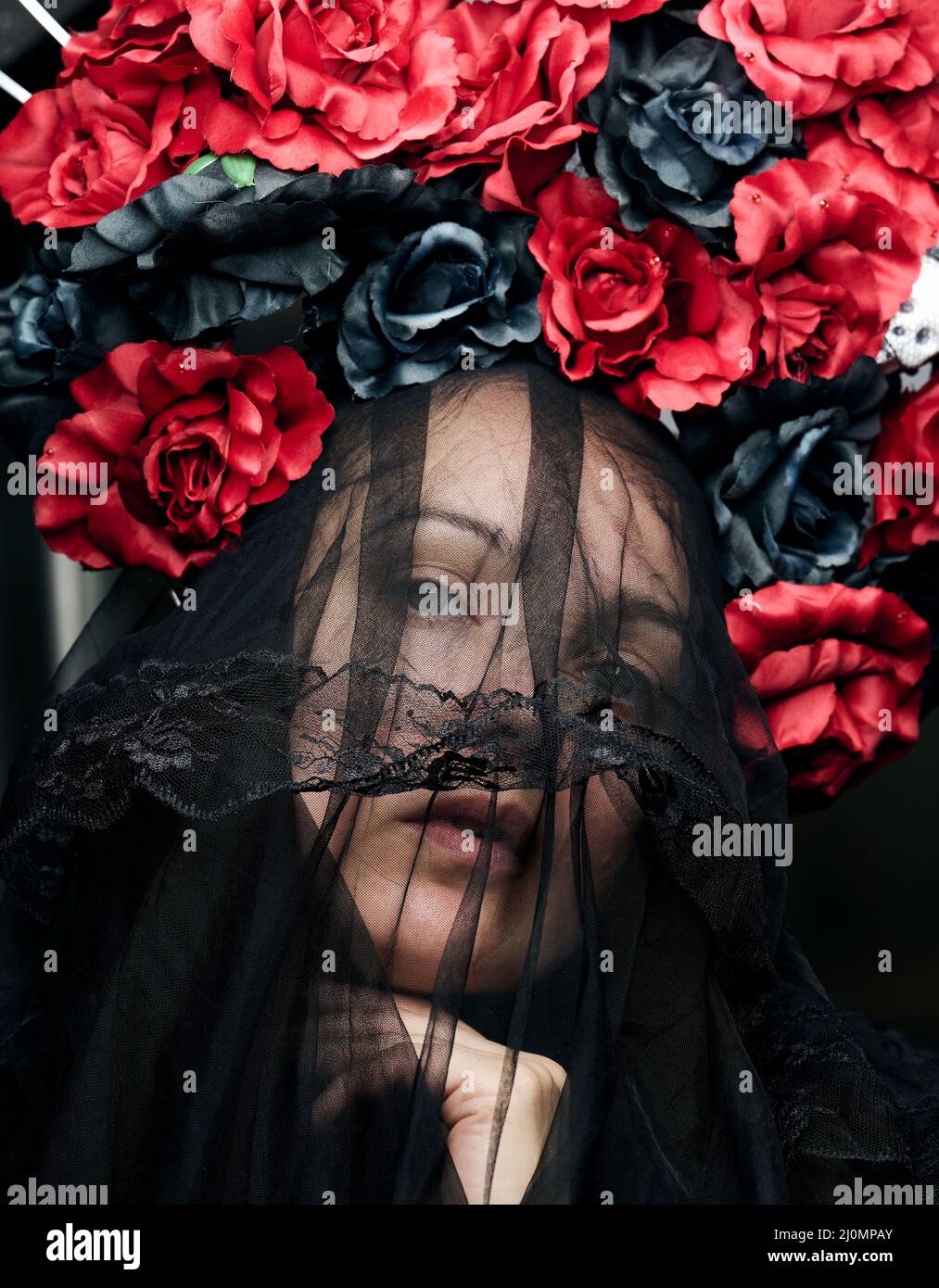 Una mujer de apariencia caucásica está vestida con un velo negro y una gran corona de rosas de color rojo y negro Foto de stock