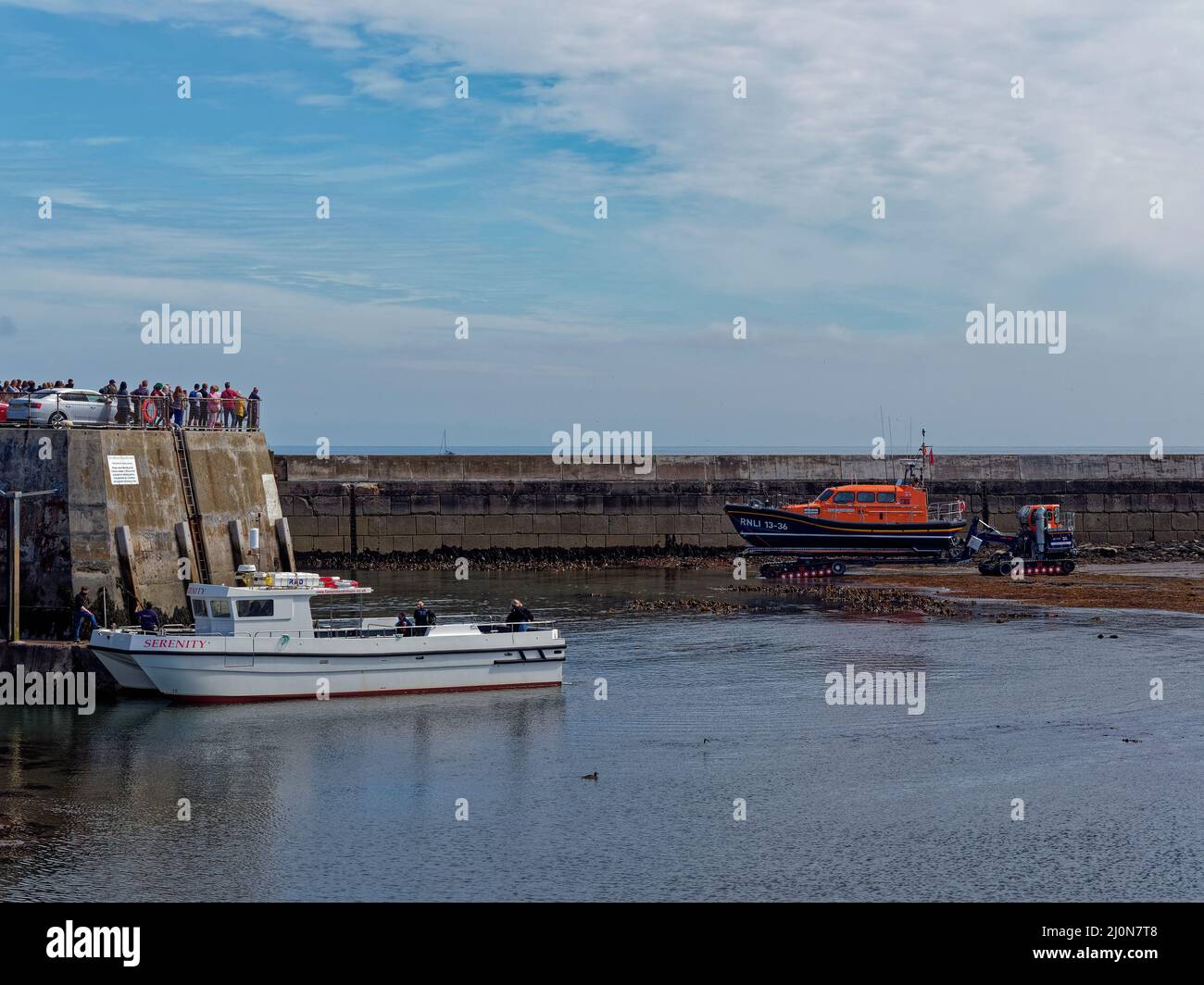 El vehículo de lanzamiento SLARS Lifeboat pasa por la embarcación Serenity Pleasure Craft en la entrada del puerto Seahouses. Foto de stock