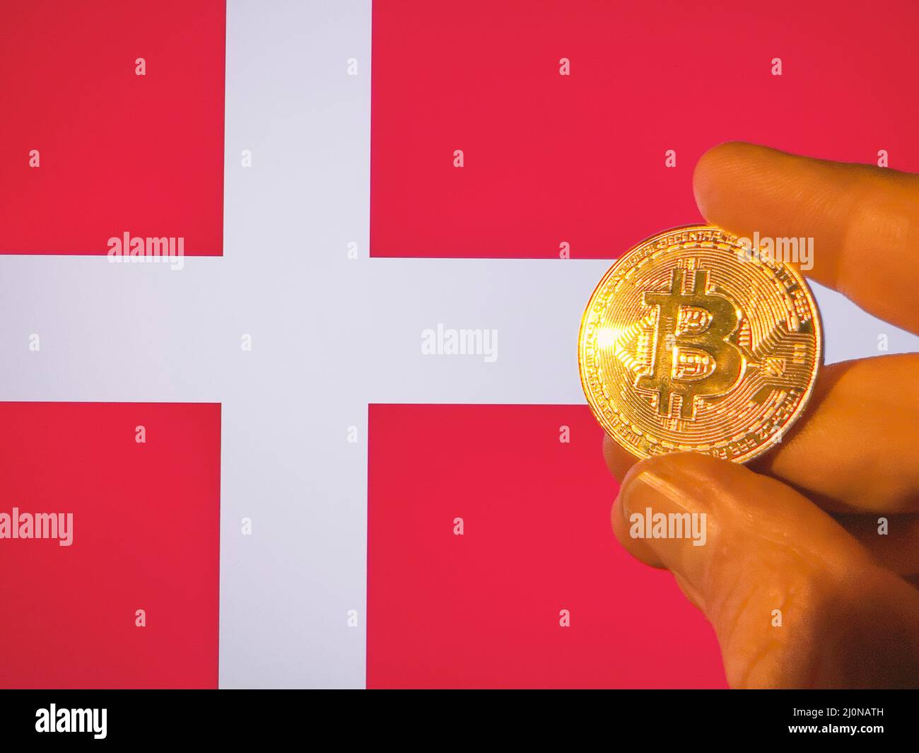 Sosteniendo un bitcoin dorado sobre la bandera danesa. Dinamarca como inversionista de tecnología de criptomoneda y blockchain. Antecedentes financieros Foto de stock