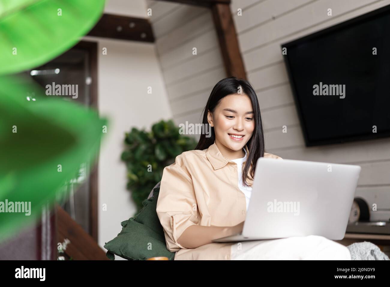 Imagen de una mujer asiática que trabaja en un ordenador portátil desde un acogedor salón. Niña estudiando haciendo la tarea en casa Foto de stock