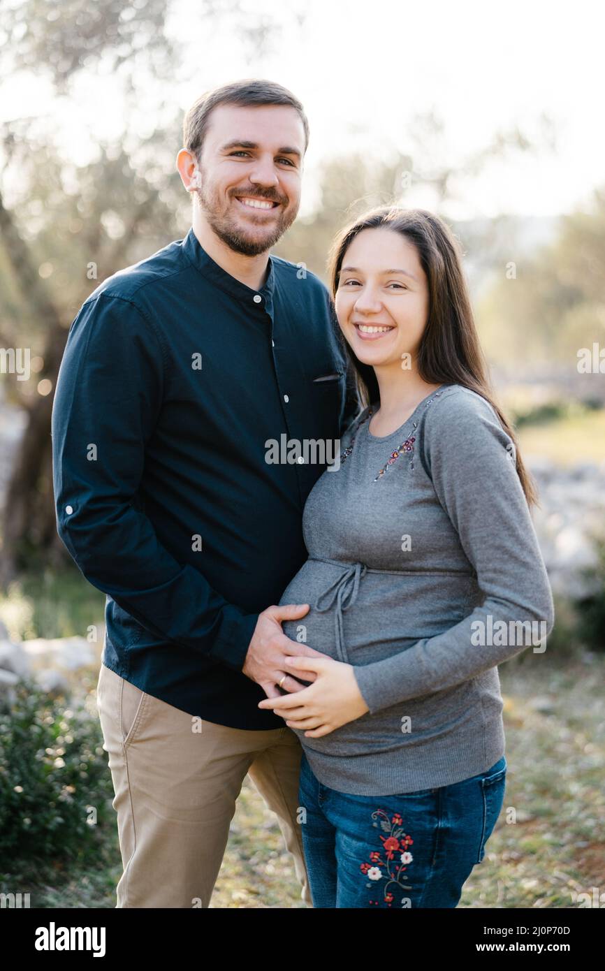 Hombre sonriente sosteniendo las manos en el vientre de una mujer embarazada Foto de stock