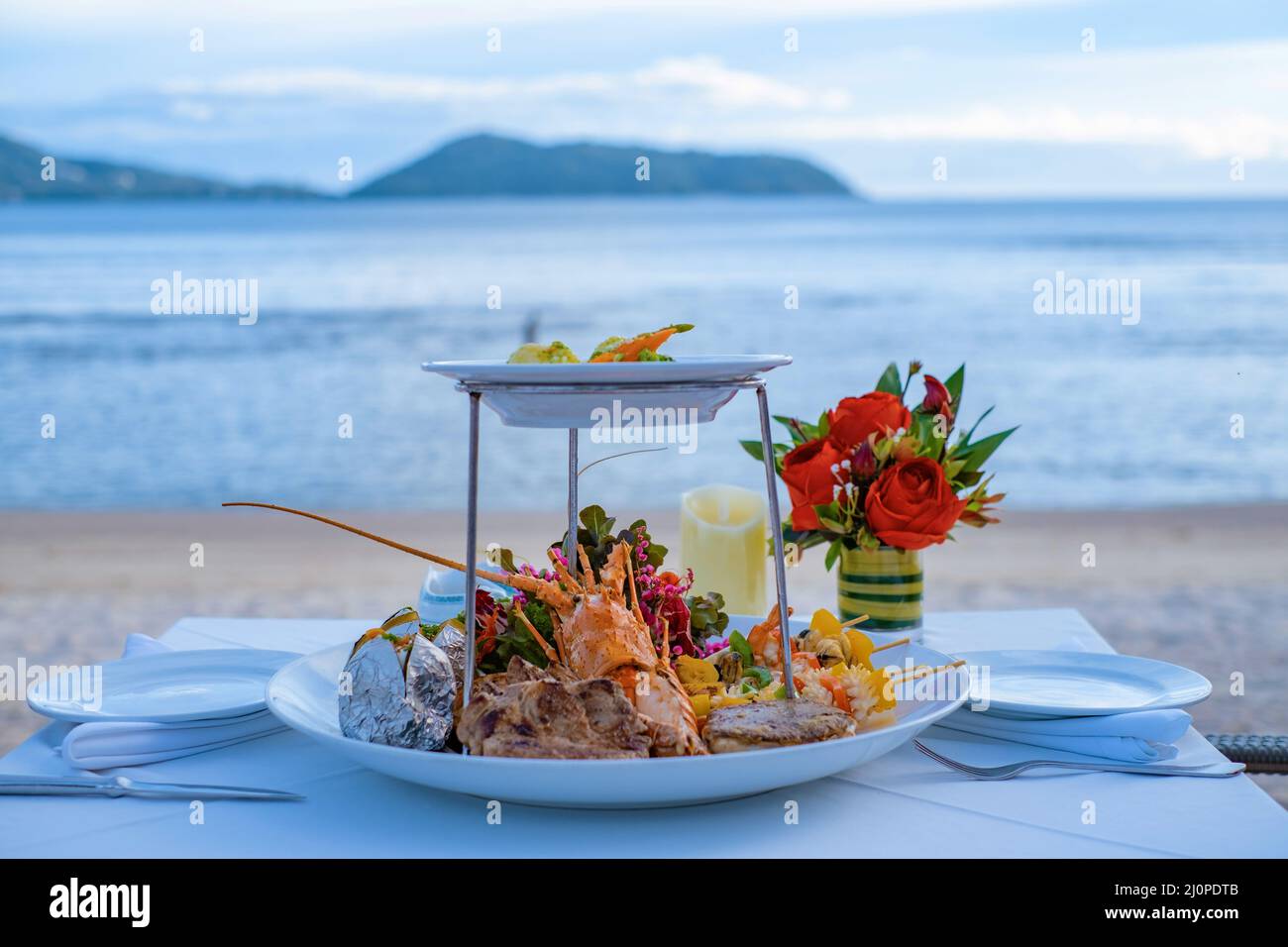 Cena romántica en la playa con langosta, marisco, carne y ensalada Foto de stock