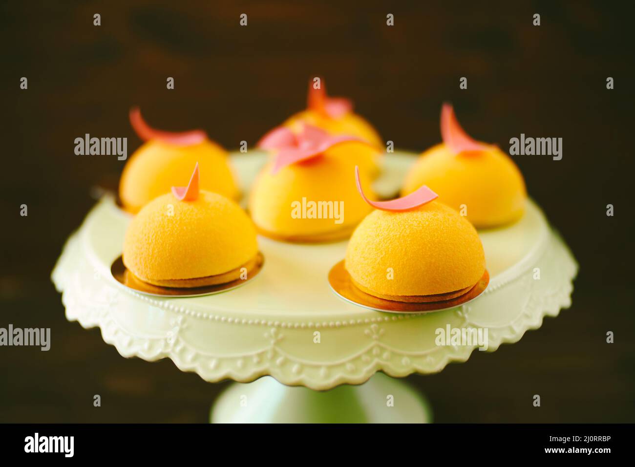 Seis tortas de mousse amarillas individuales decoradas con flores vidriadas sobre una mesa giratoria Foto de stock