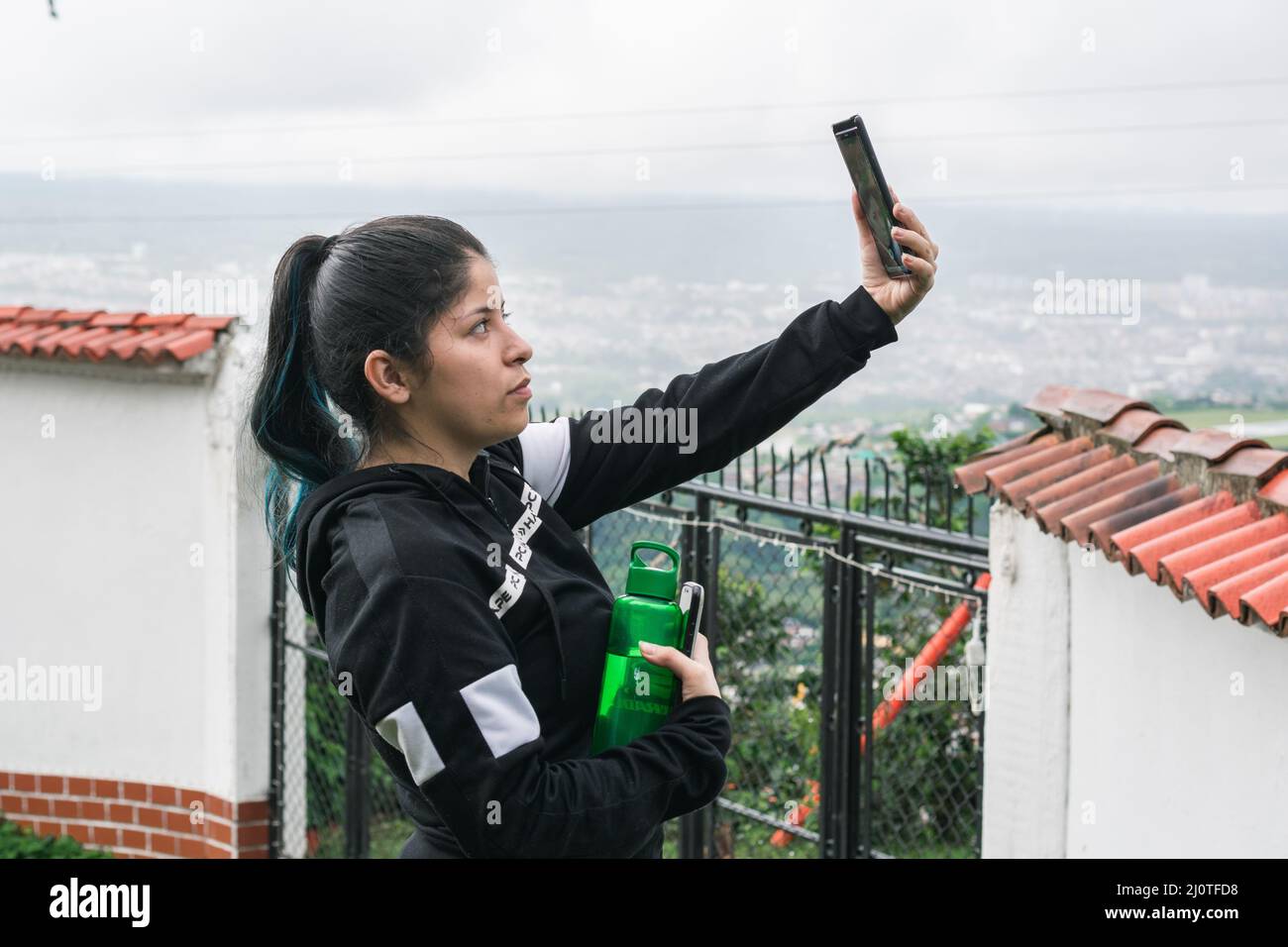 joven latina tomando un selfie con su ropa deportiva y un termo para el  agua en su mano. Chica haciendo ejercicio en una mañana fría cerca de la  ciudad de Pereira-Colom Fotografía