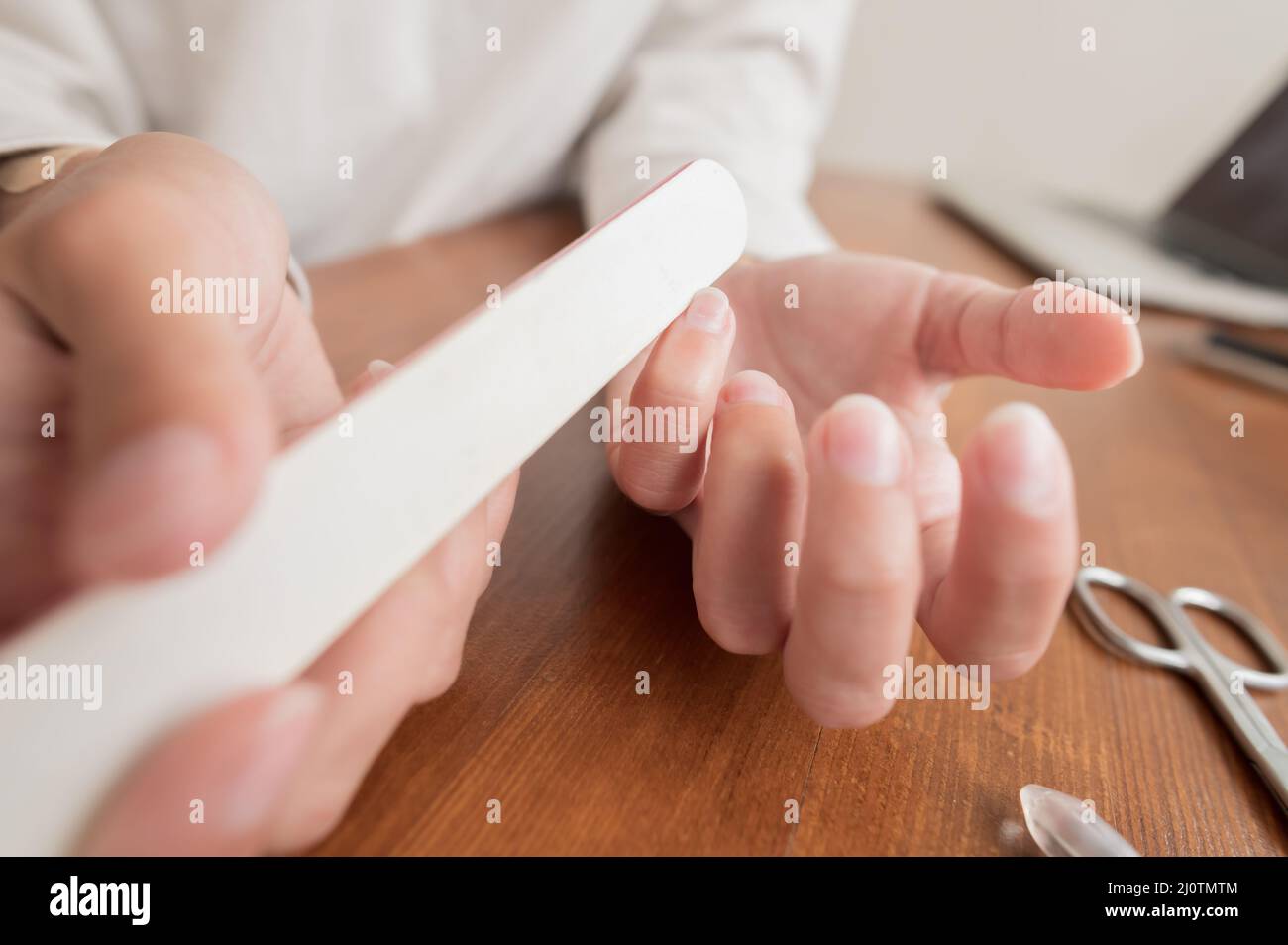 La mano femenina de una niña archiva clavos con un archivo de uñas en la mesa. Manicura en casa Foto de stock