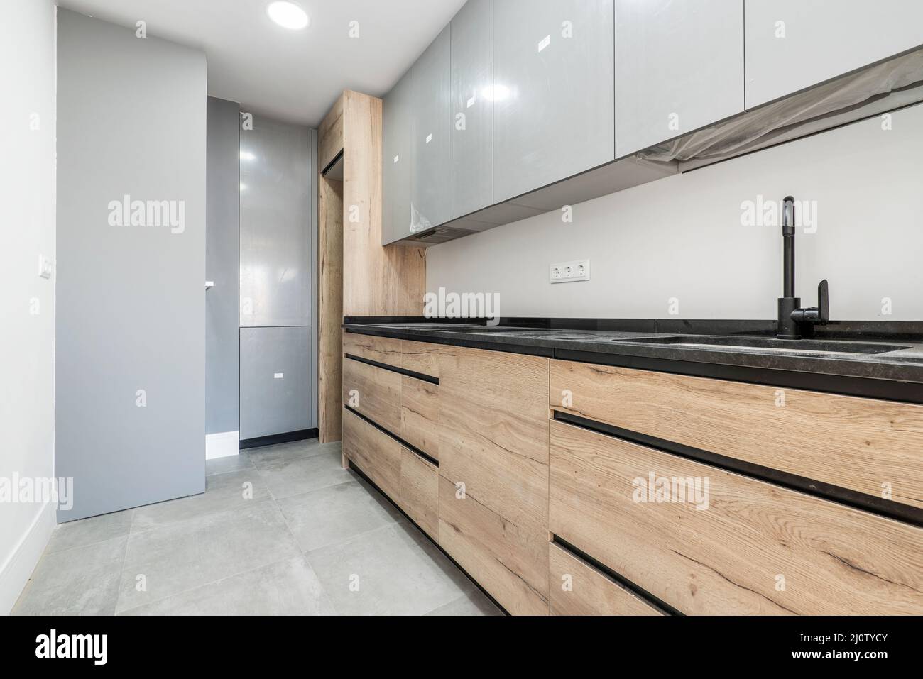 Cocina con muebles de madera combinados con puertas grises en las columnas  y encimera de piedra negra brillante, grifo negro y pisos de gres gris  Fotografía de stock - Alamy